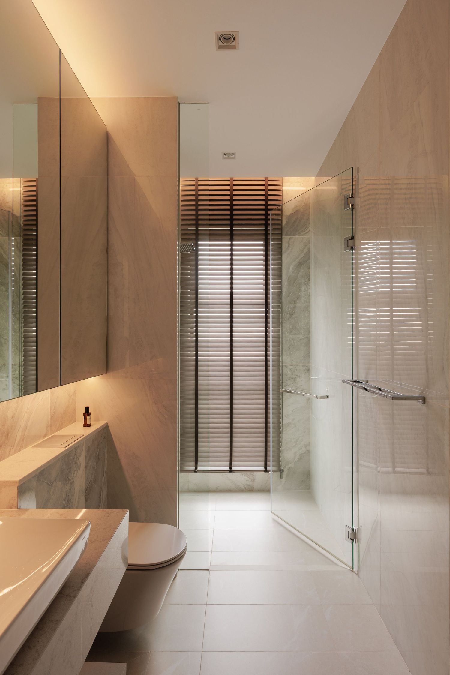 Modern minimalist bathroom features floating vanity, marble walls, and horizontal window blinds creating clean lines and elegance.