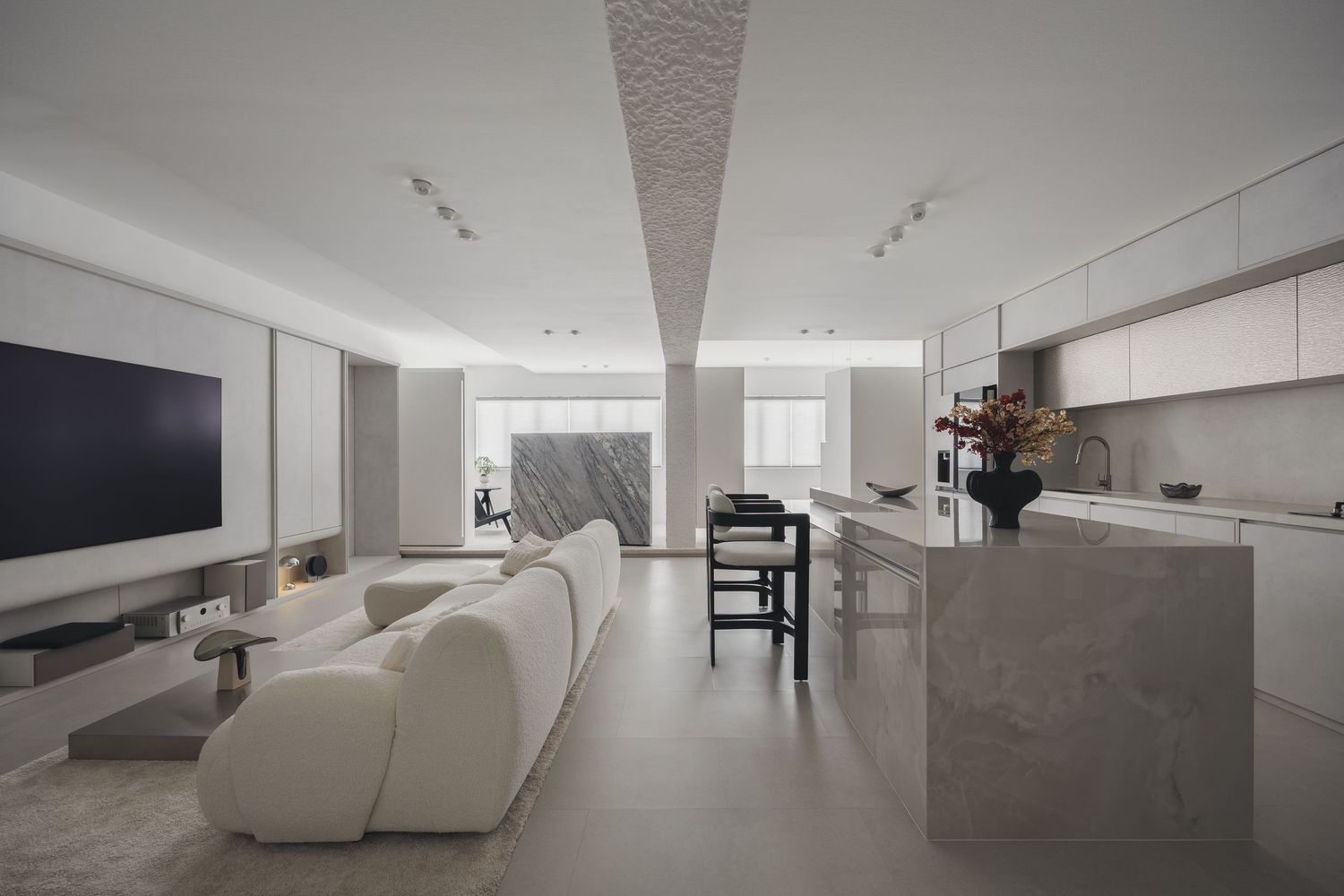 Modern open-plan living space with white sofa, marble kitchen island, large TV, and minimalist decor in neutral tones.