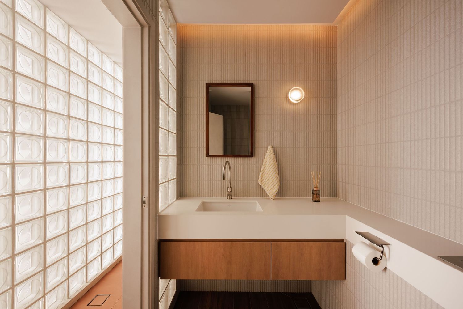 Modern bathroom interior with glass block wall, recessed lighting, and minimalist white fixtures.