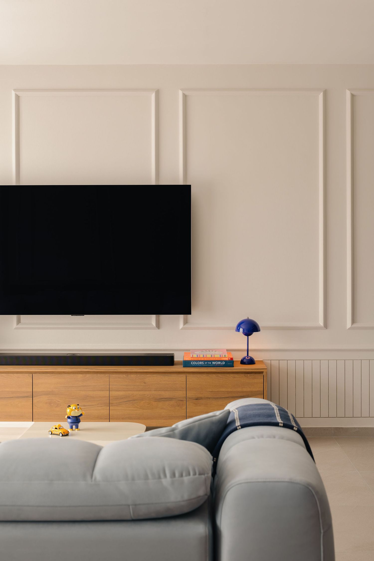 Modern living room with gray sofa, wall-mounted TV, wooden media console, and elegant white wainscoting wall panels.