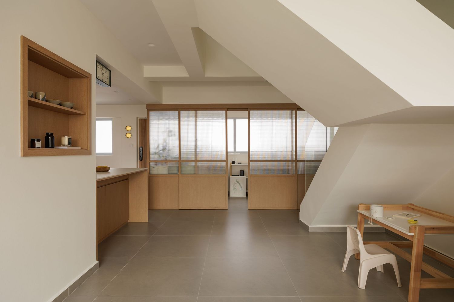Minimalist attic room with wooden built-ins, sloped ceiling, and large windows offering natural light.