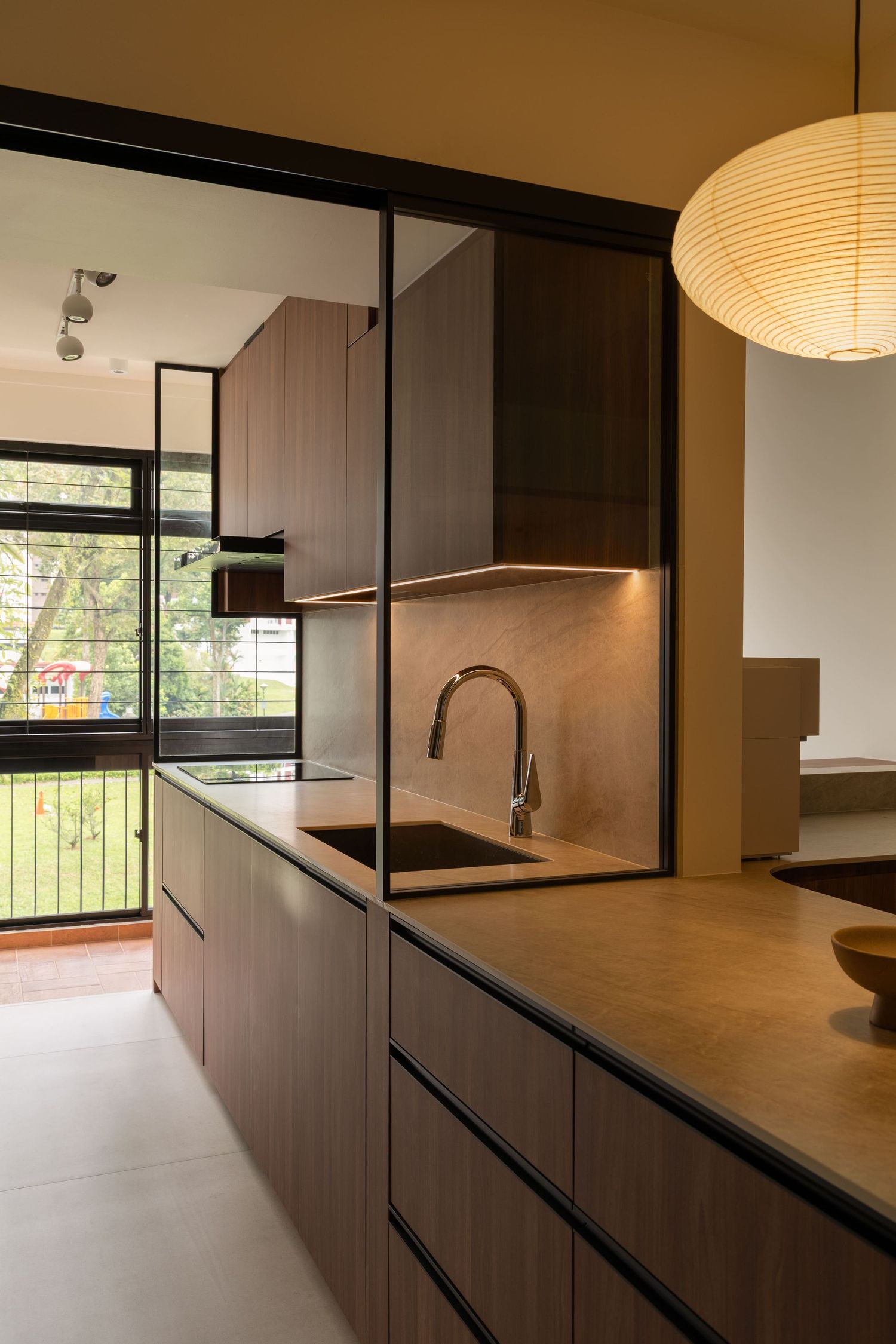 Modern kitchen interior with dark wood cabinets, pendant lighting, and sleek countertops in a minimalist design.