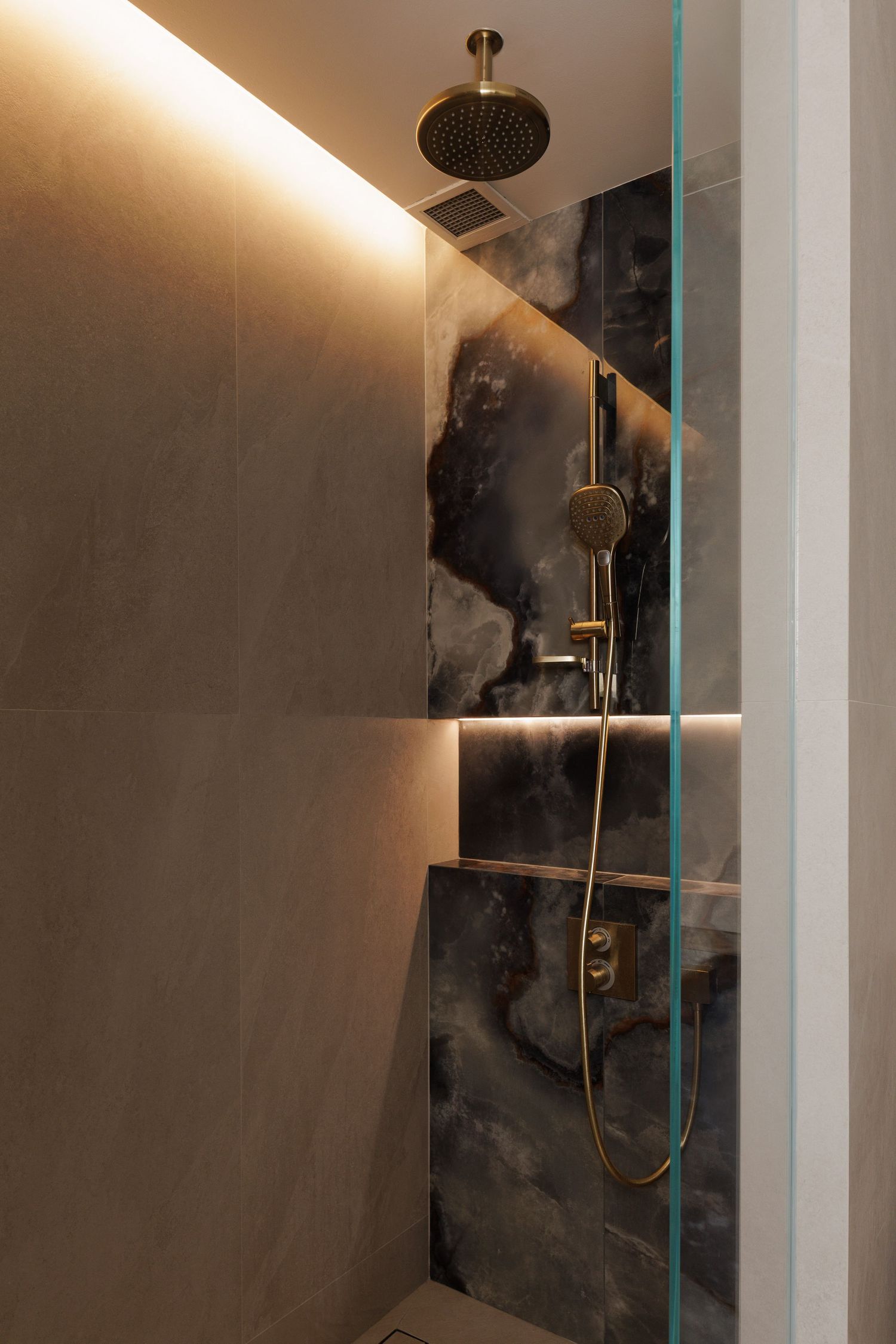 Modern luxury shower with black marble accent wall, brass fixtures, and hidden LED lighting creates an elegant spa-like atmosphere.