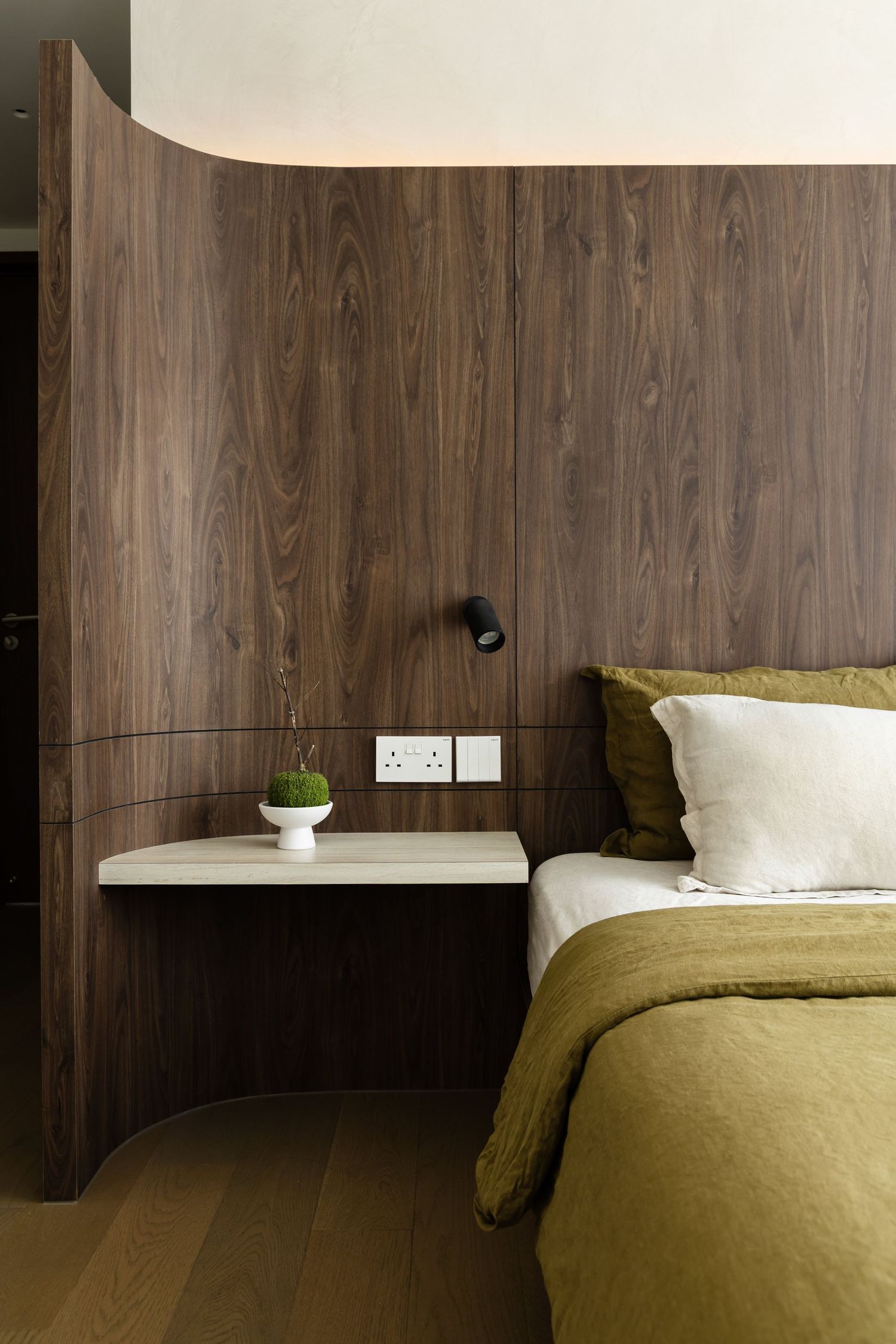 Contemporary bedroom interior with wooden walls and olive green bedding showcases minimalist floating nightstands and outlets.