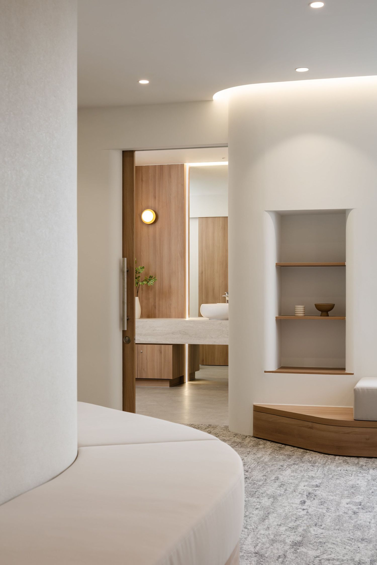 Modern minimalist bathroom interior with curved walls, wooden accents, and built-in shelving features soft recessed lighting.