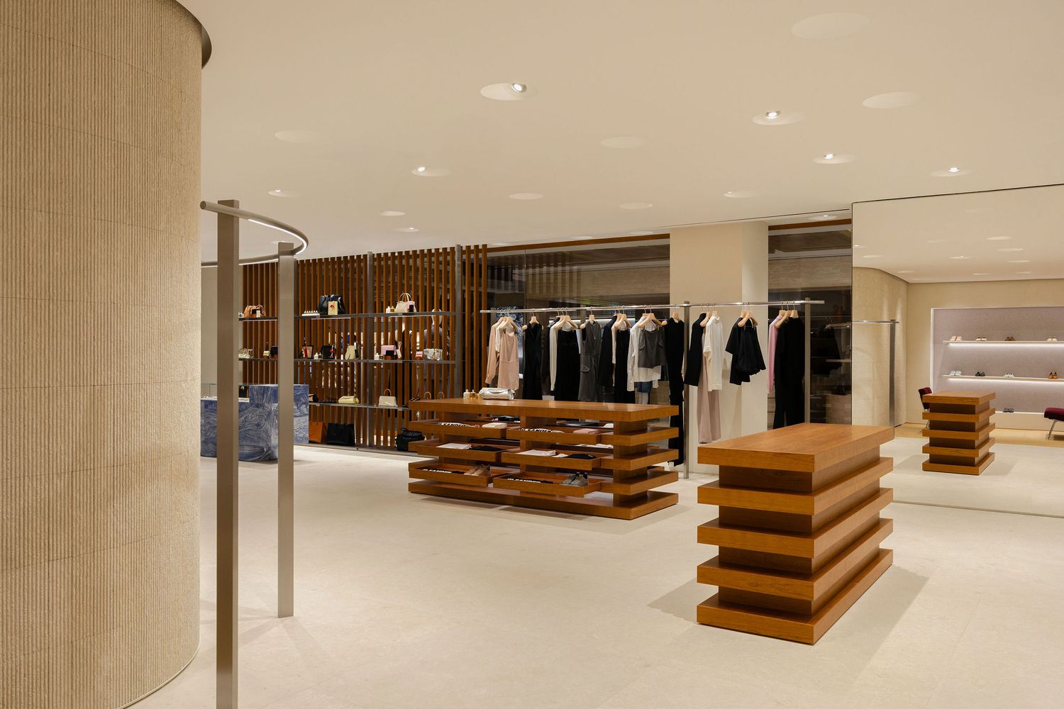 Modern luxury retail store interior with wooden display tables, clothing racks, and elegant beige flooring under recessed lighting.