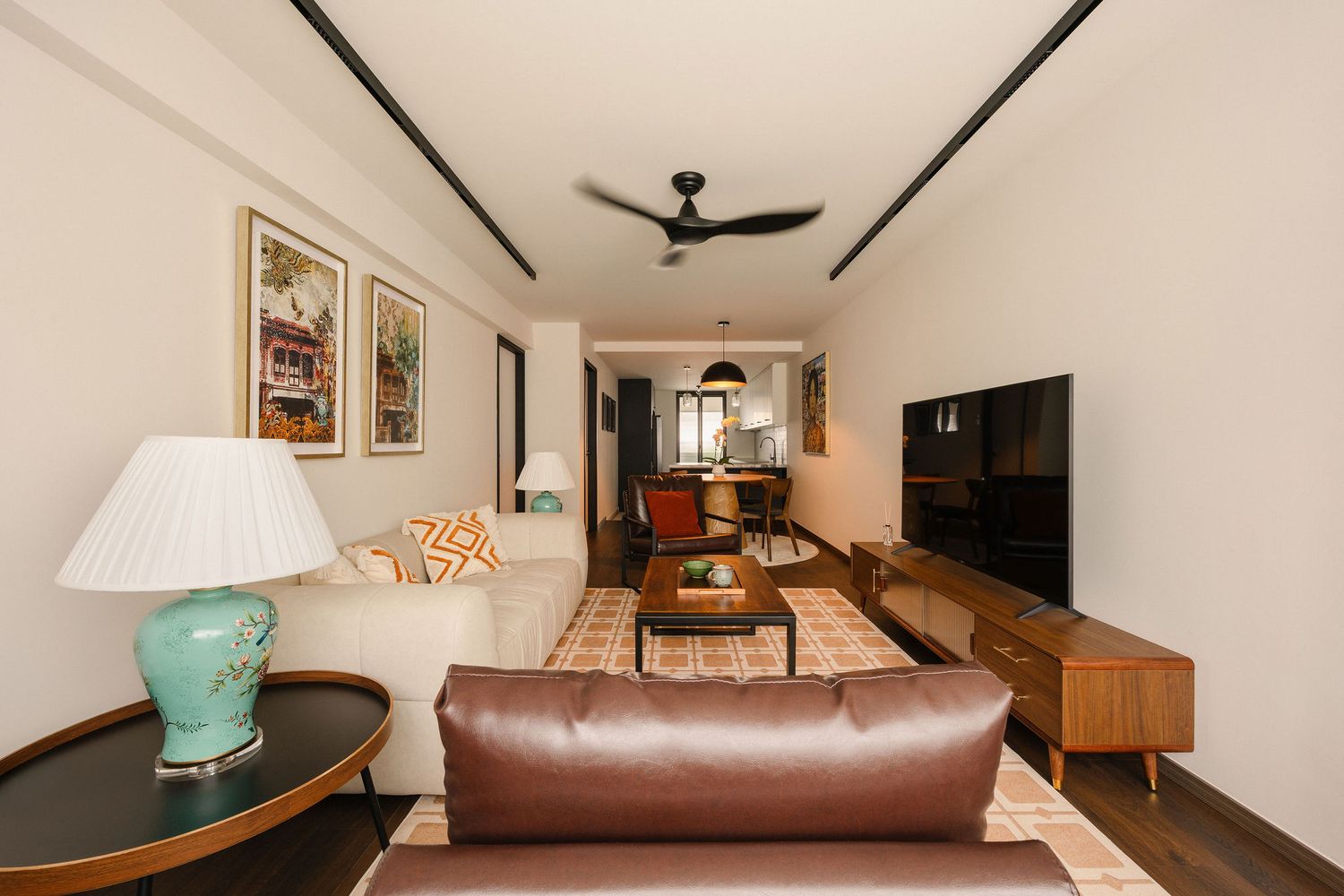 Modern living room with leather sofa, teal lamp, wooden TV console, ceiling fan, and warm patterned rug in neutral tones.