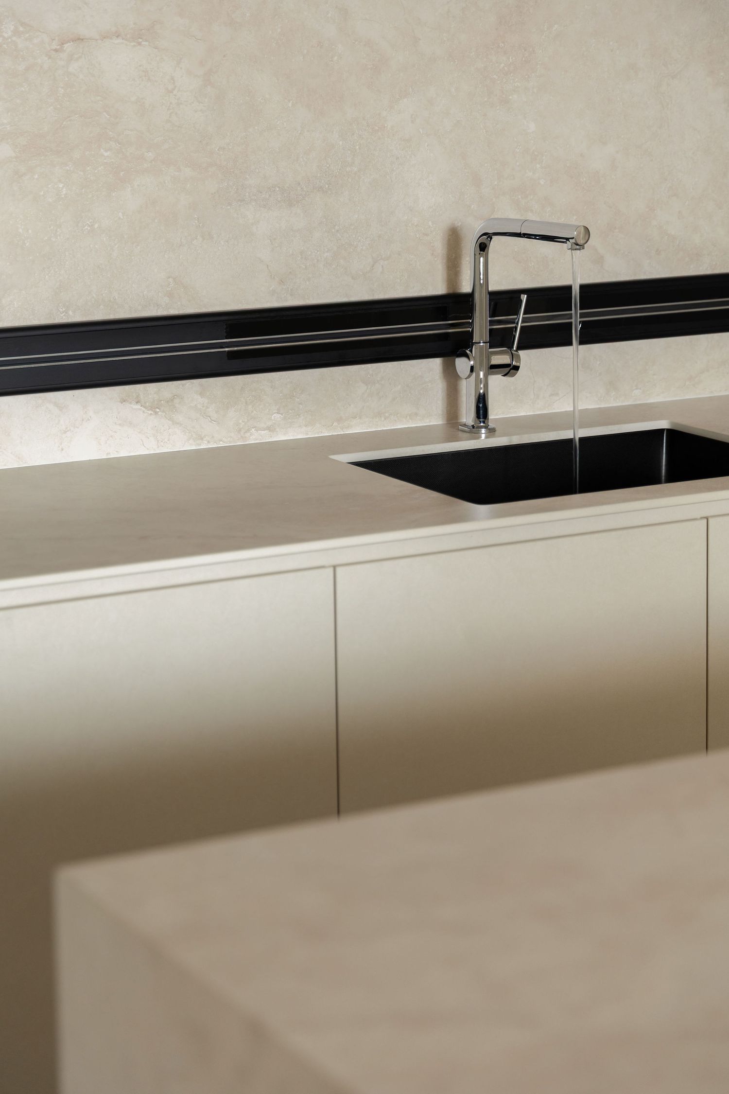 Modern minimalist kitchen with black undermount sink, chrome faucet, beige cabinetry, and marble backsplash.