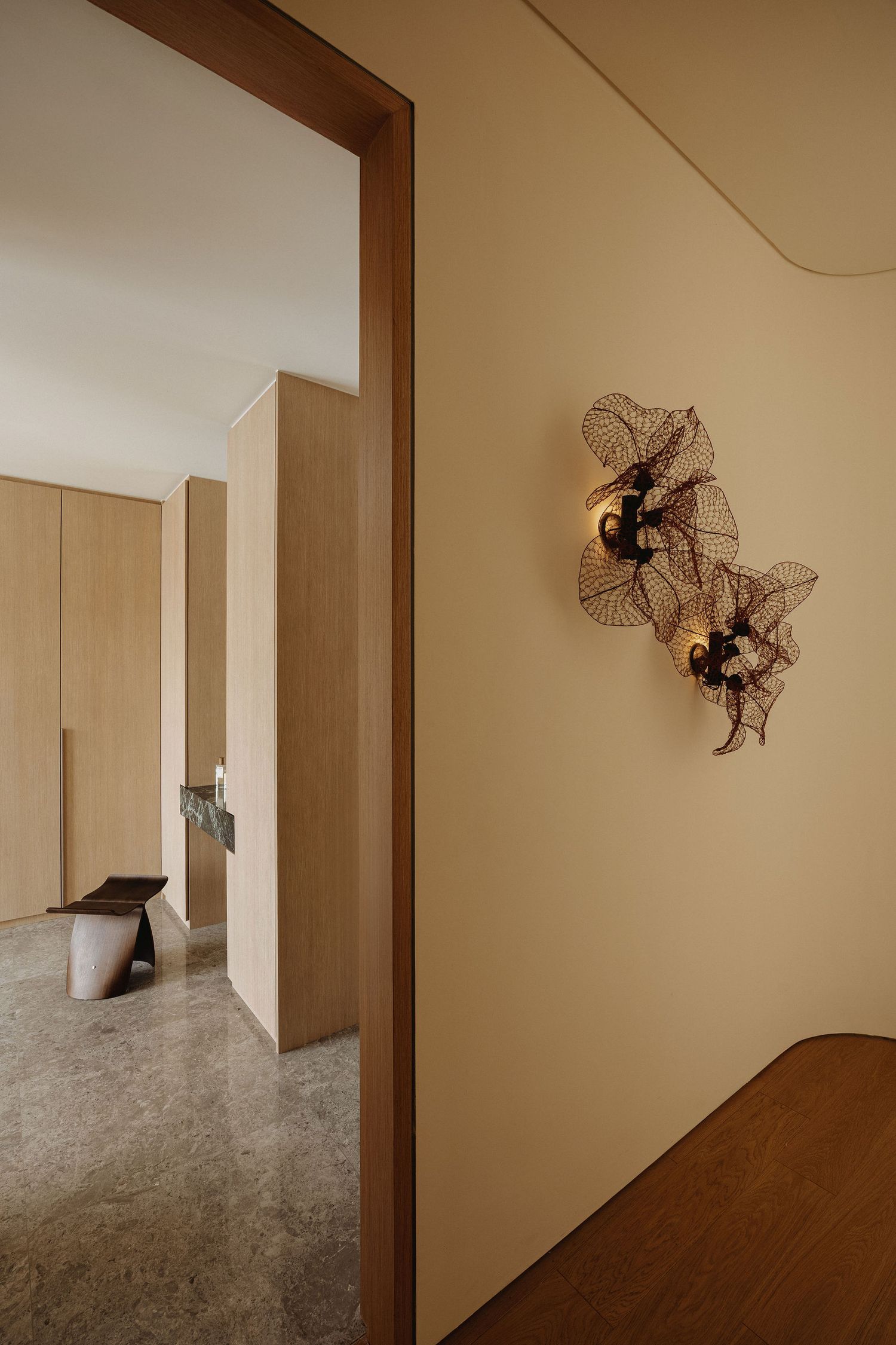 Modern hallway with warm beige walls, wood-framed doorway, and decorative wire leaf wall sconces.