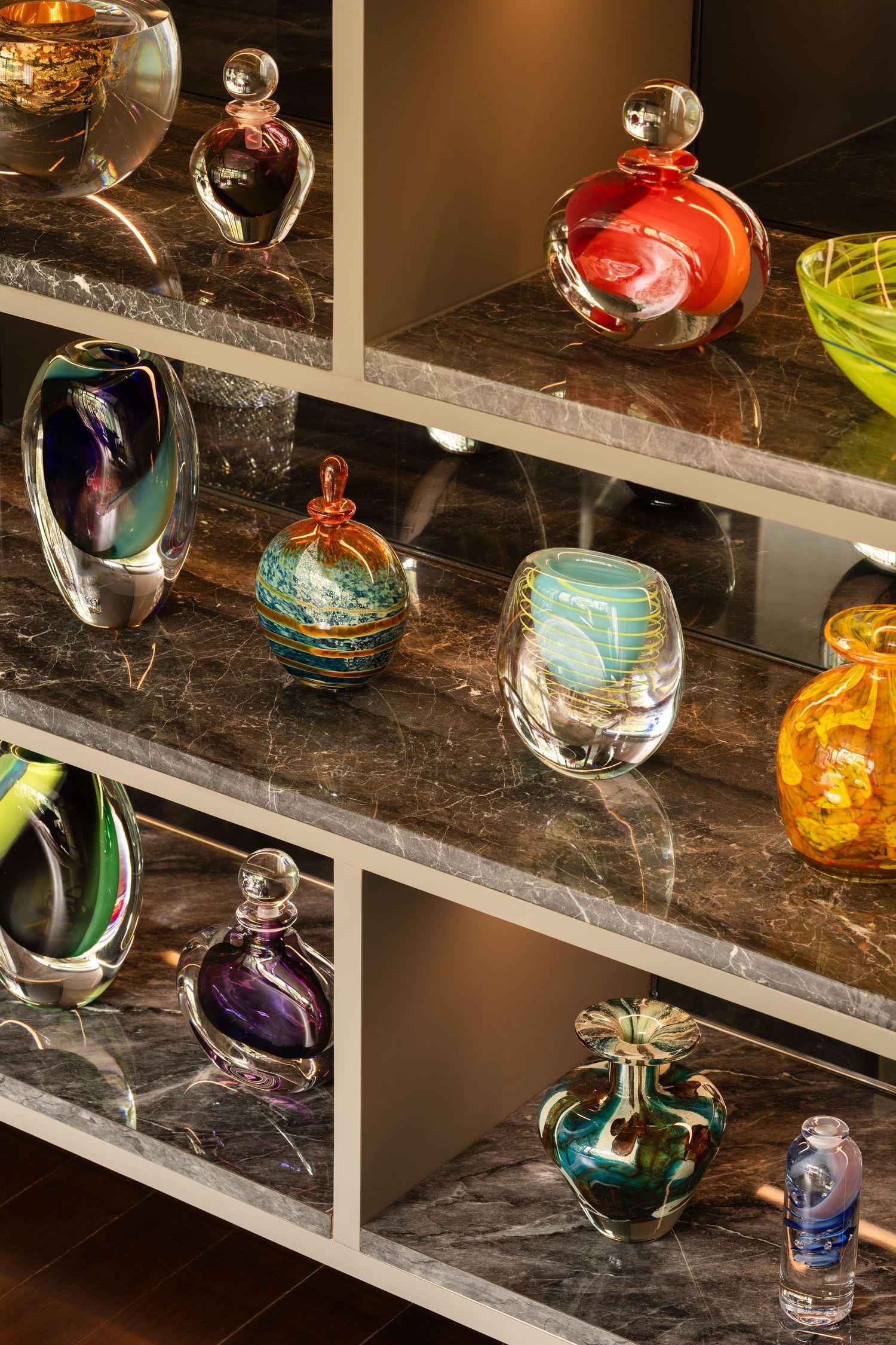 Beautiful handblown glass ornaments in various colors displayed on marble shelves with soft lighting.