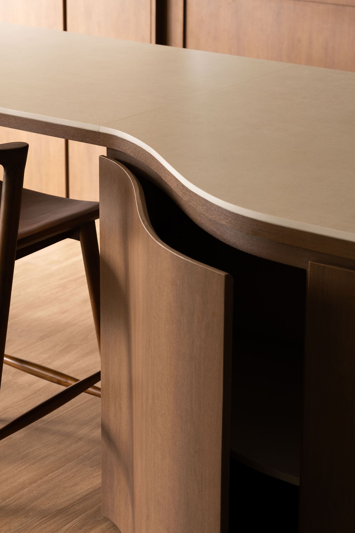 Close-up detail of modern light wood dining table with curved edges and clean lines against hardwood flooring.