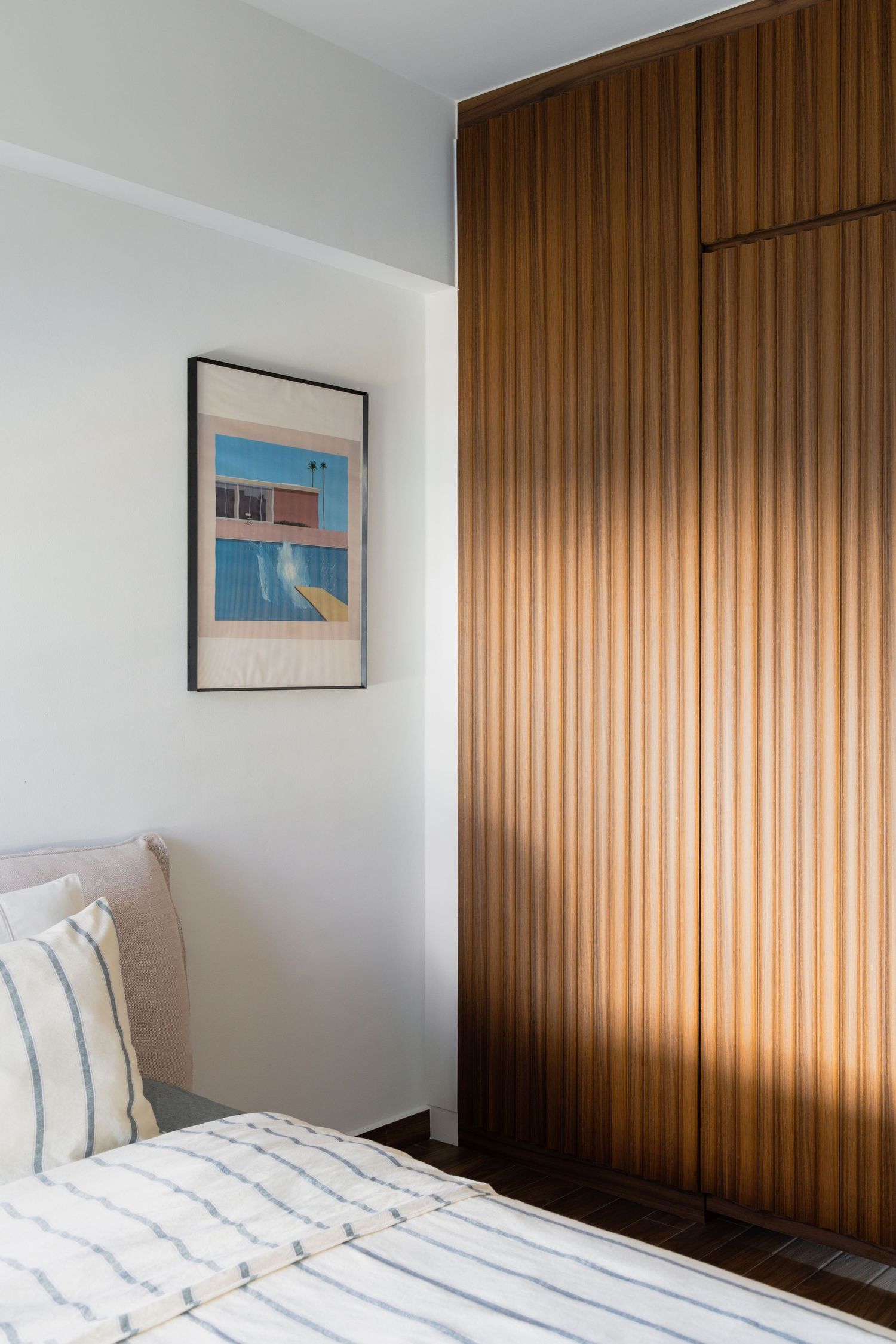 A minimalist bedroom interior features warm wood paneling, white bedding, and simple wall art against white walls.