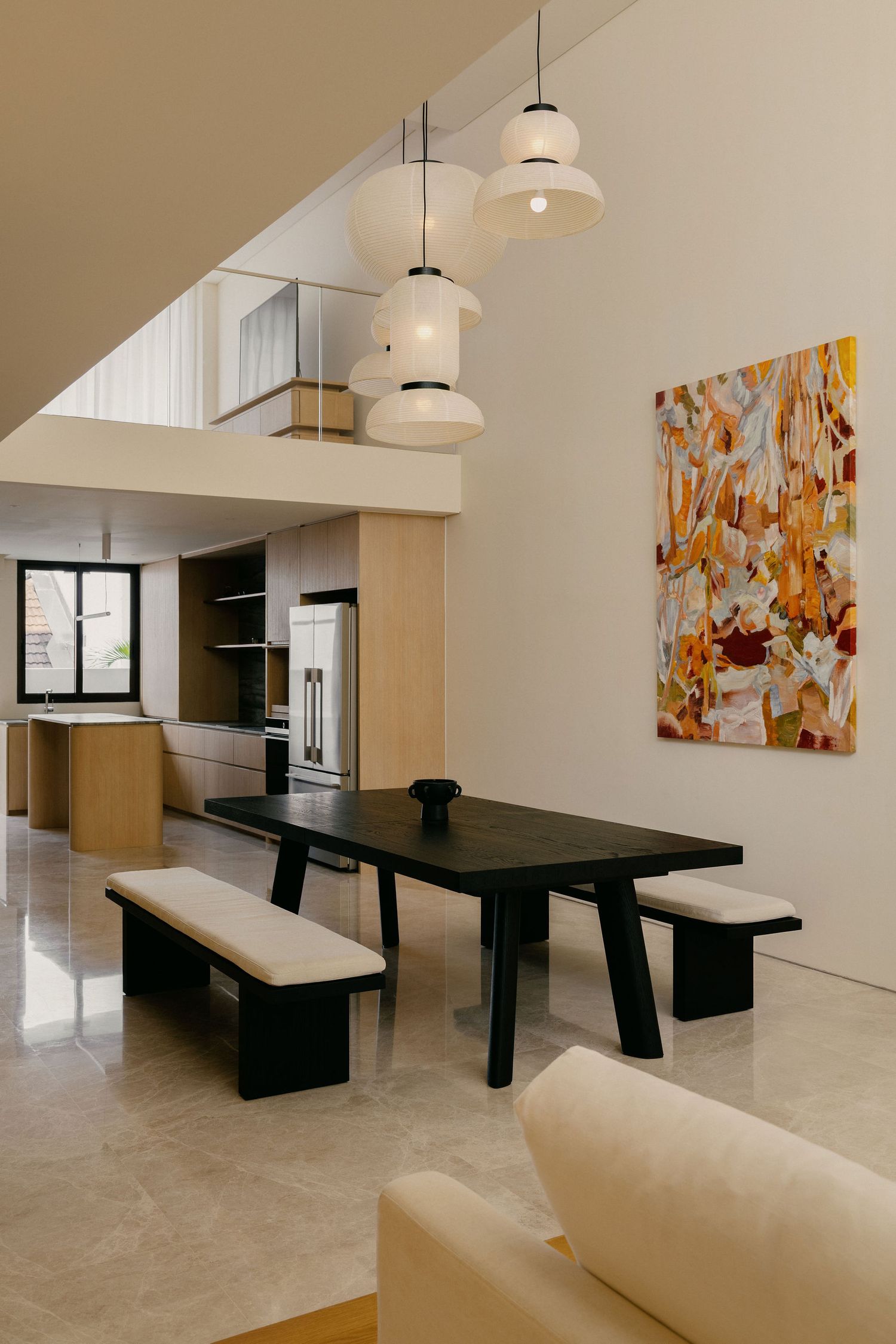 Modern dining room with black table, benches, pendant lights, abstract wall art, and open kitchen in neutral tones.