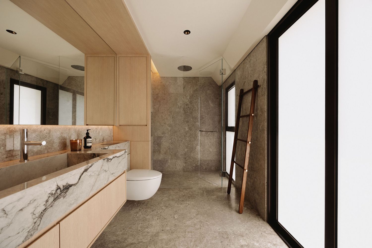 Modern bathroom with marble vanity, wood cabinetry, gray stone walls, walk-in shower, and wooden ladder accent.