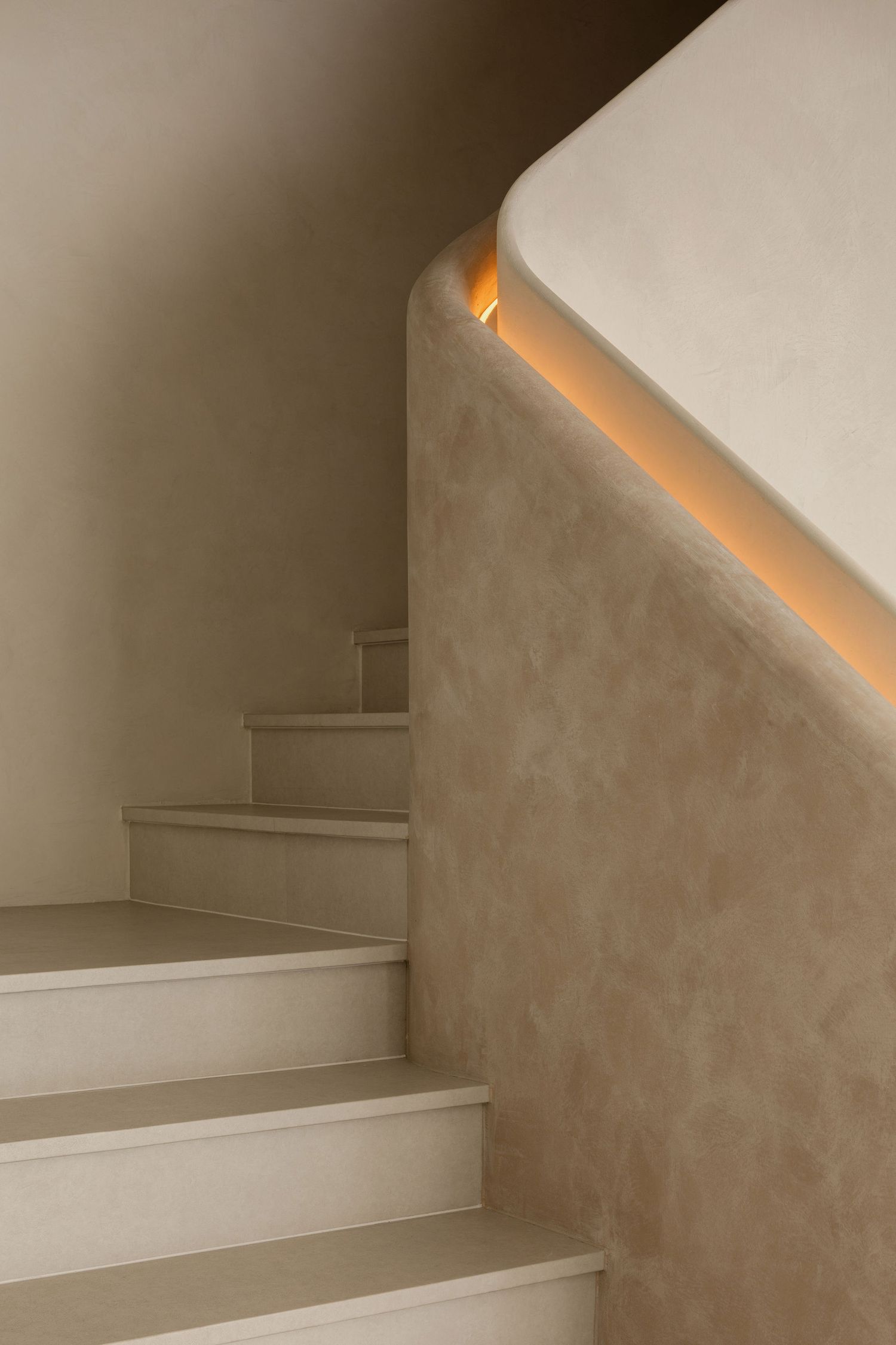 Modern staircase with warm LED strip lighting under curved handrail, neutral beige plaster walls.