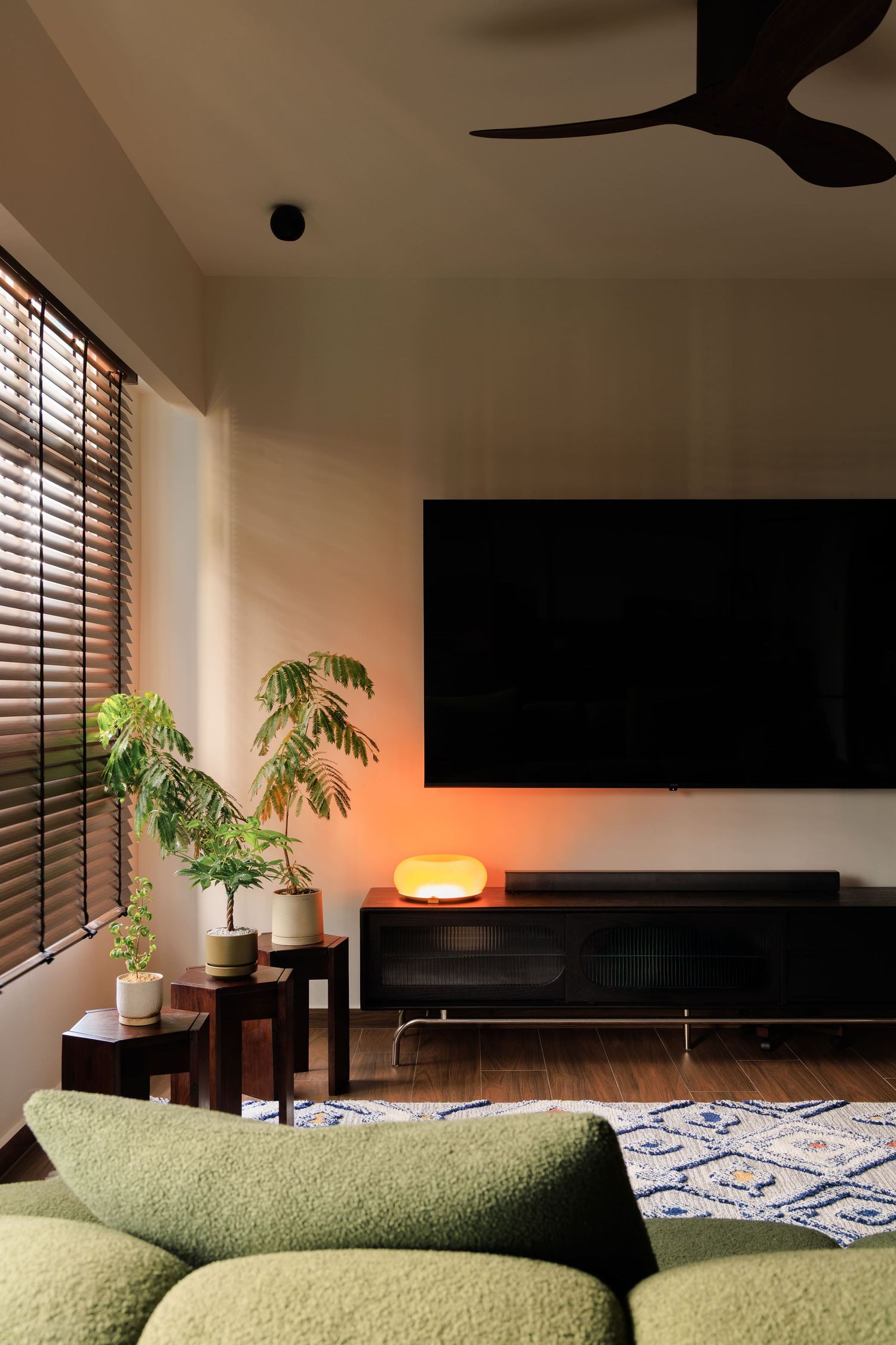 Modern living room interior with green sofa, potted plants, and ambient lighting creating a cozy atmosphere.