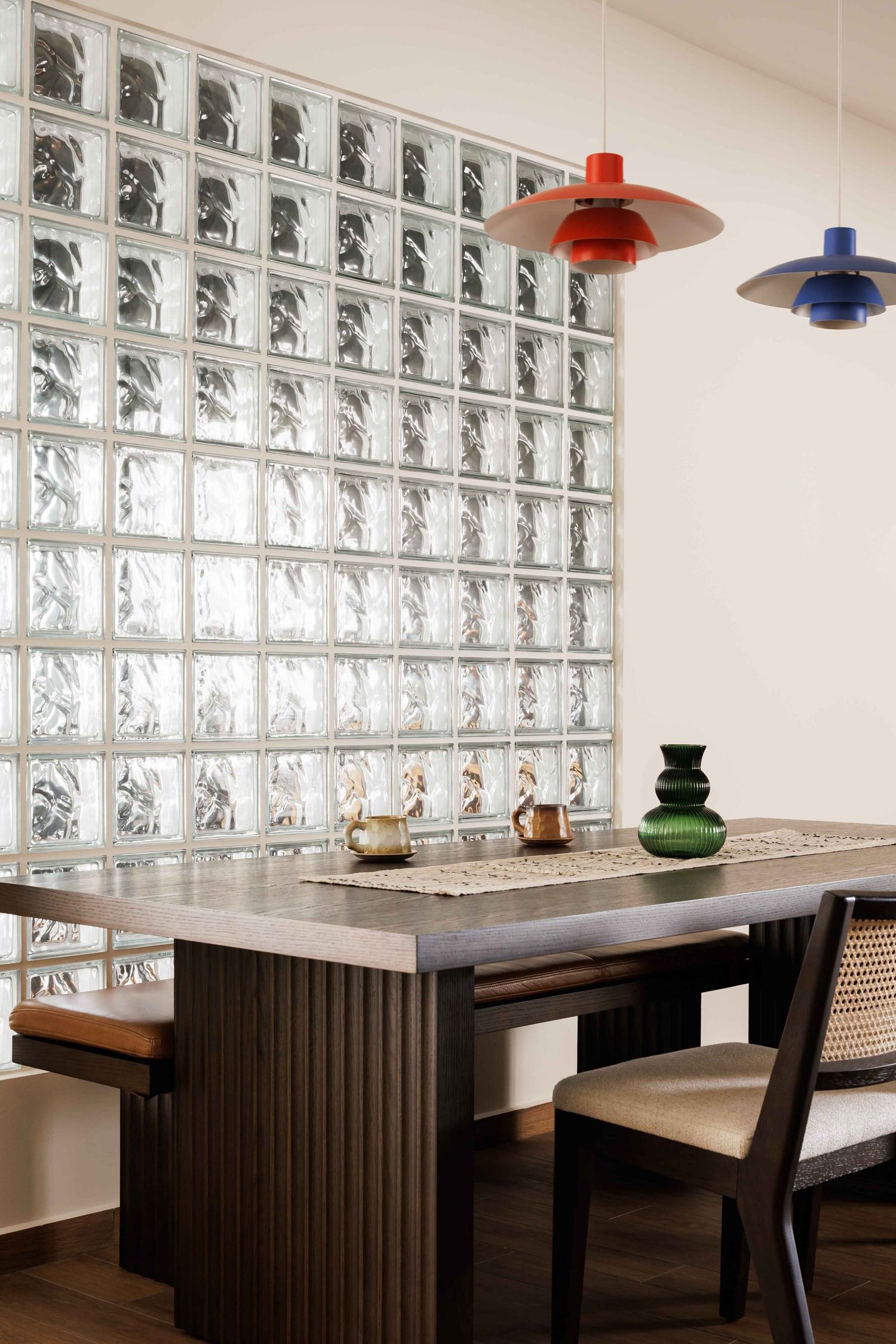 Modern restaurant interior with glass block wall, dark wood tables and colorful pendant lights creating an elegant dining space.