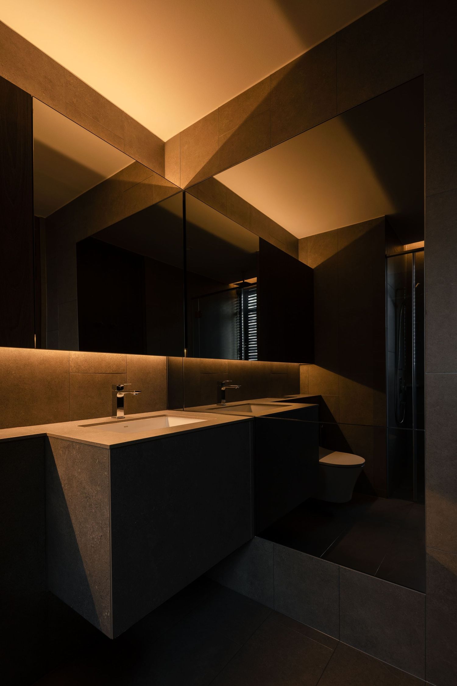 Modern dark bathroom with warm amber LED lighting, geometric ceiling design, floating vanity, and large mirror.