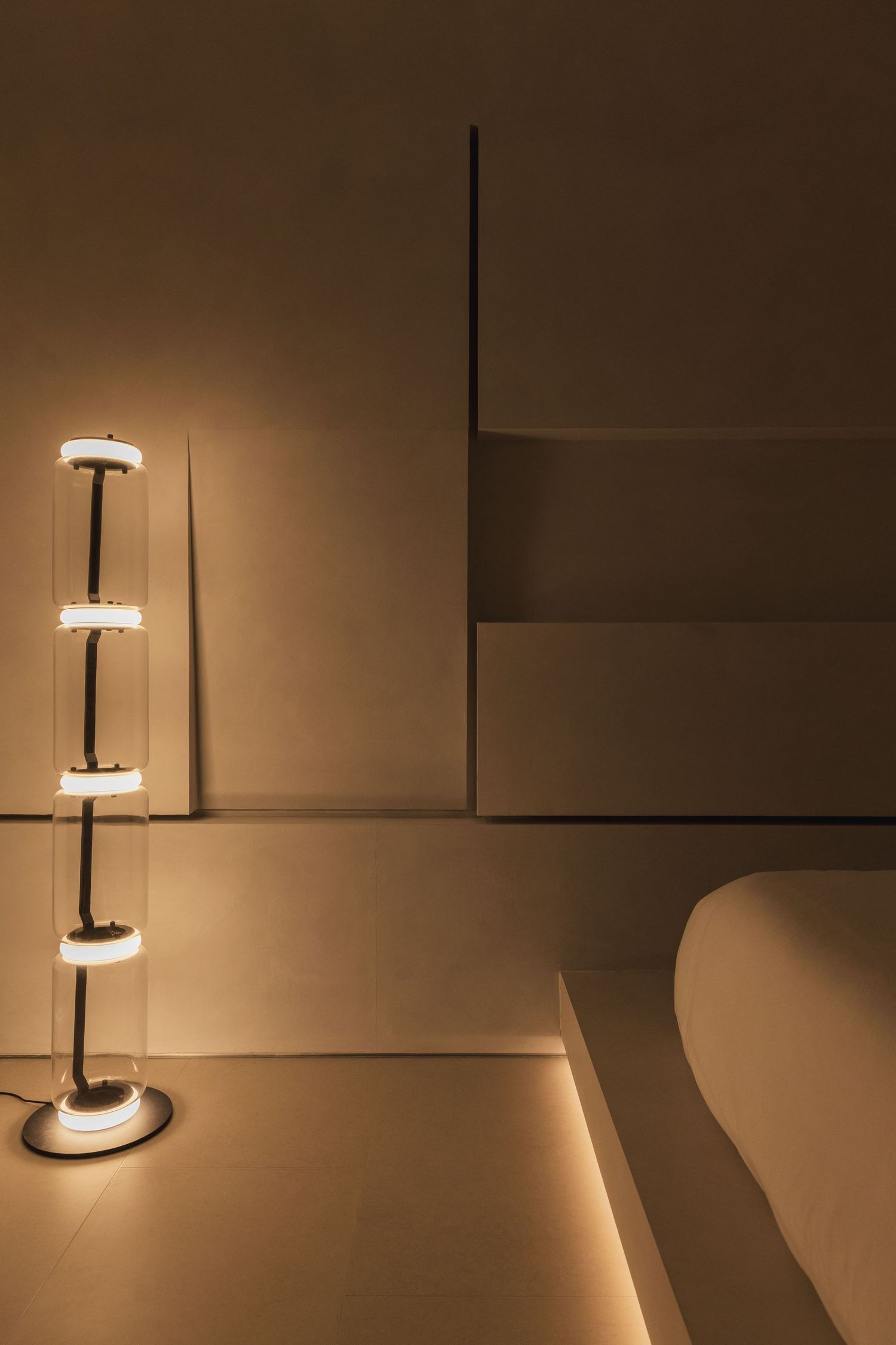 Modern floor lamp with stacked cylindrical glass shades casting warm golden light against beige architectural walls.