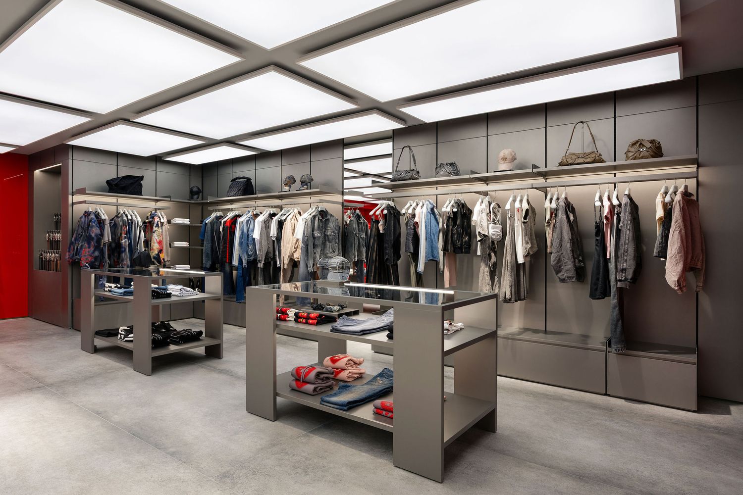 Modern boutique clothing store interior with metal shelving, hanging garments, and display cases on gray concrete floors.