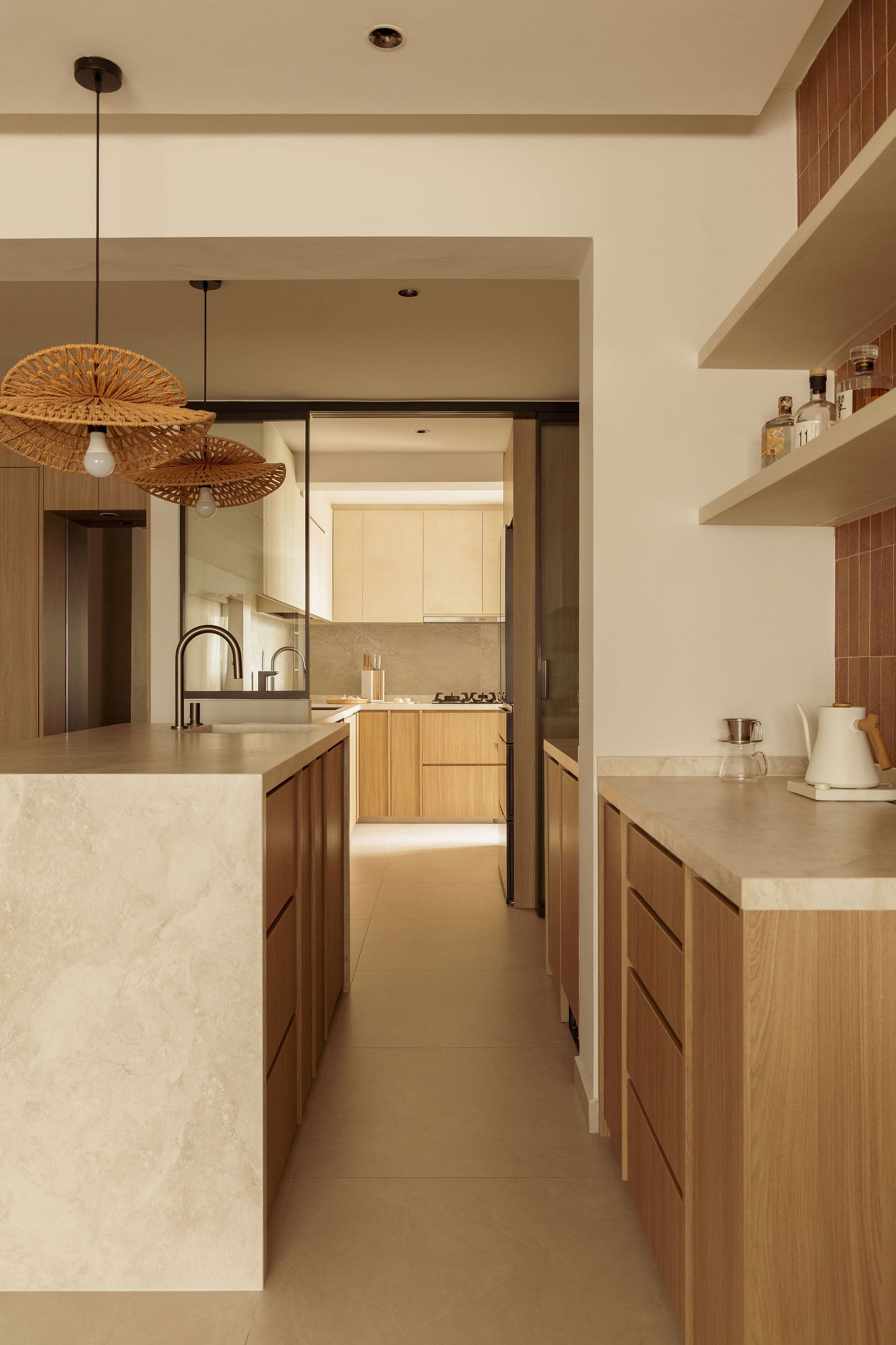 Modern kitchen with warm wood cabinetry, marble island, rattan pendant lights, and open shelving in neutral tones.