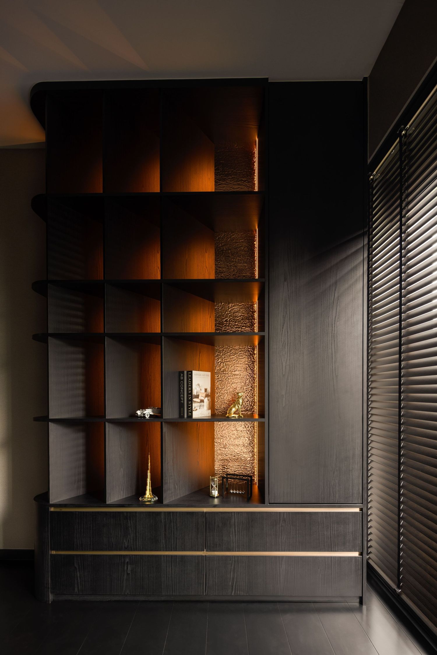 Dark luxury bookshelf with warm amber backlit compartments, gold trim drawers, and decorative accents in a modern interior.