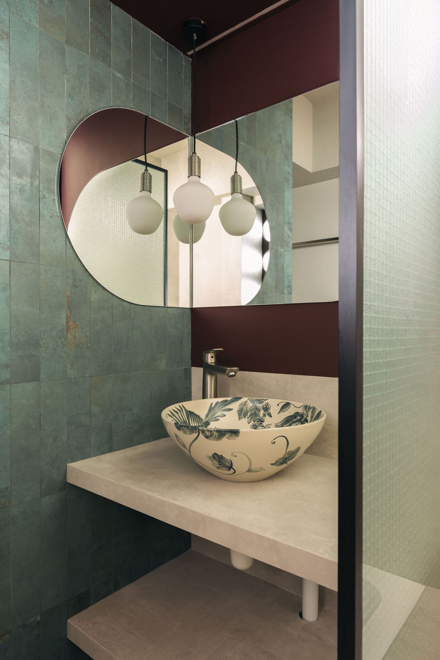 Modern bathroom with decorative bowl sink, round mirror, teal tiles, and globe pendant lights on marble vanity.