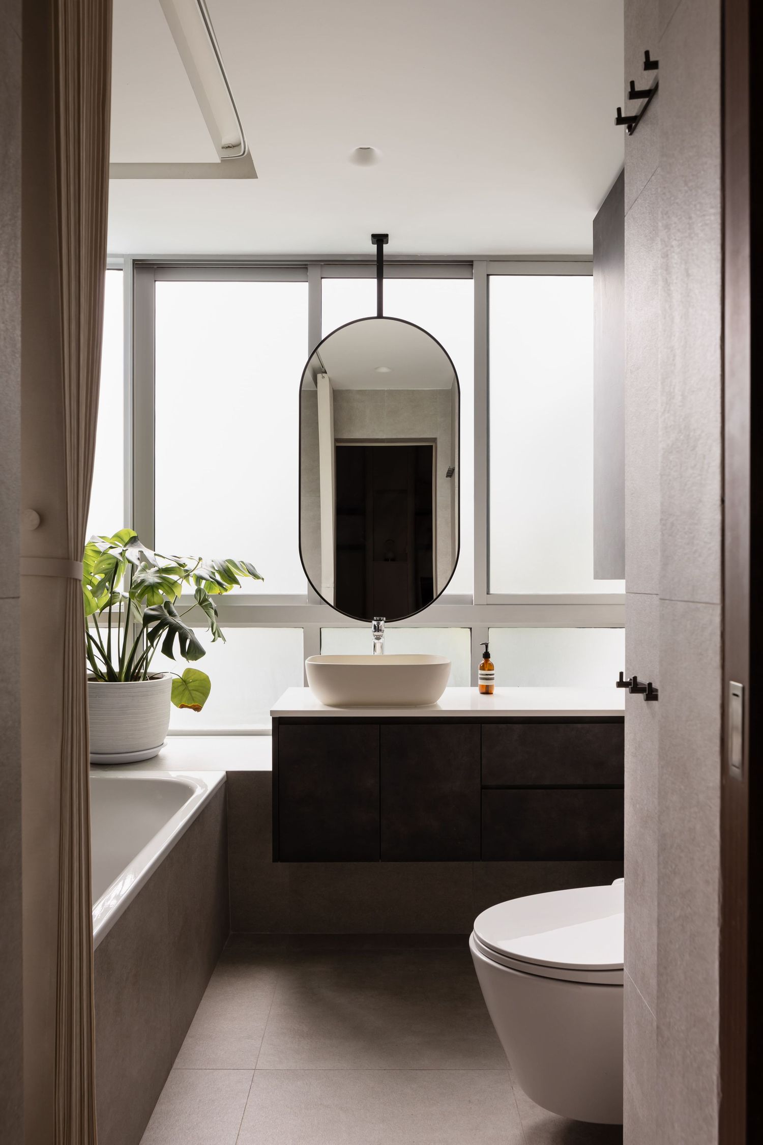 Modern minimalist bathroom interior with white fixtures, round mirror, and natural light streaming through large windows.