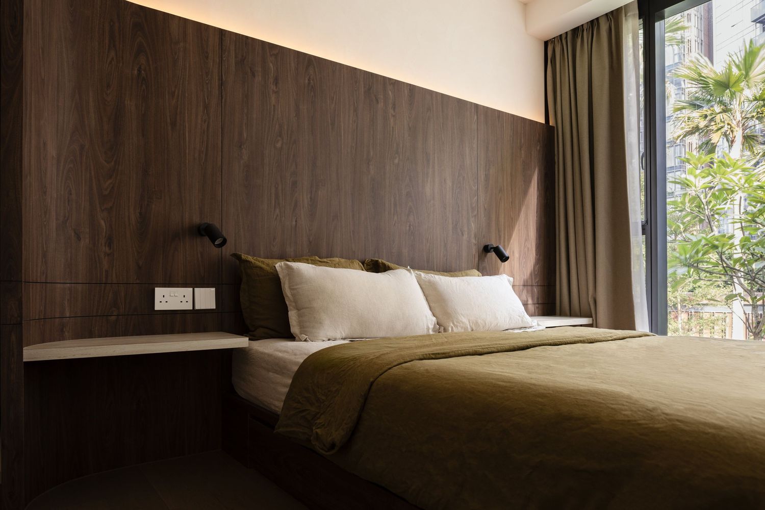 Modern bedroom interior with dark wood paneled wall, white bedding, and wall-mounted reading lamps beside a large window.