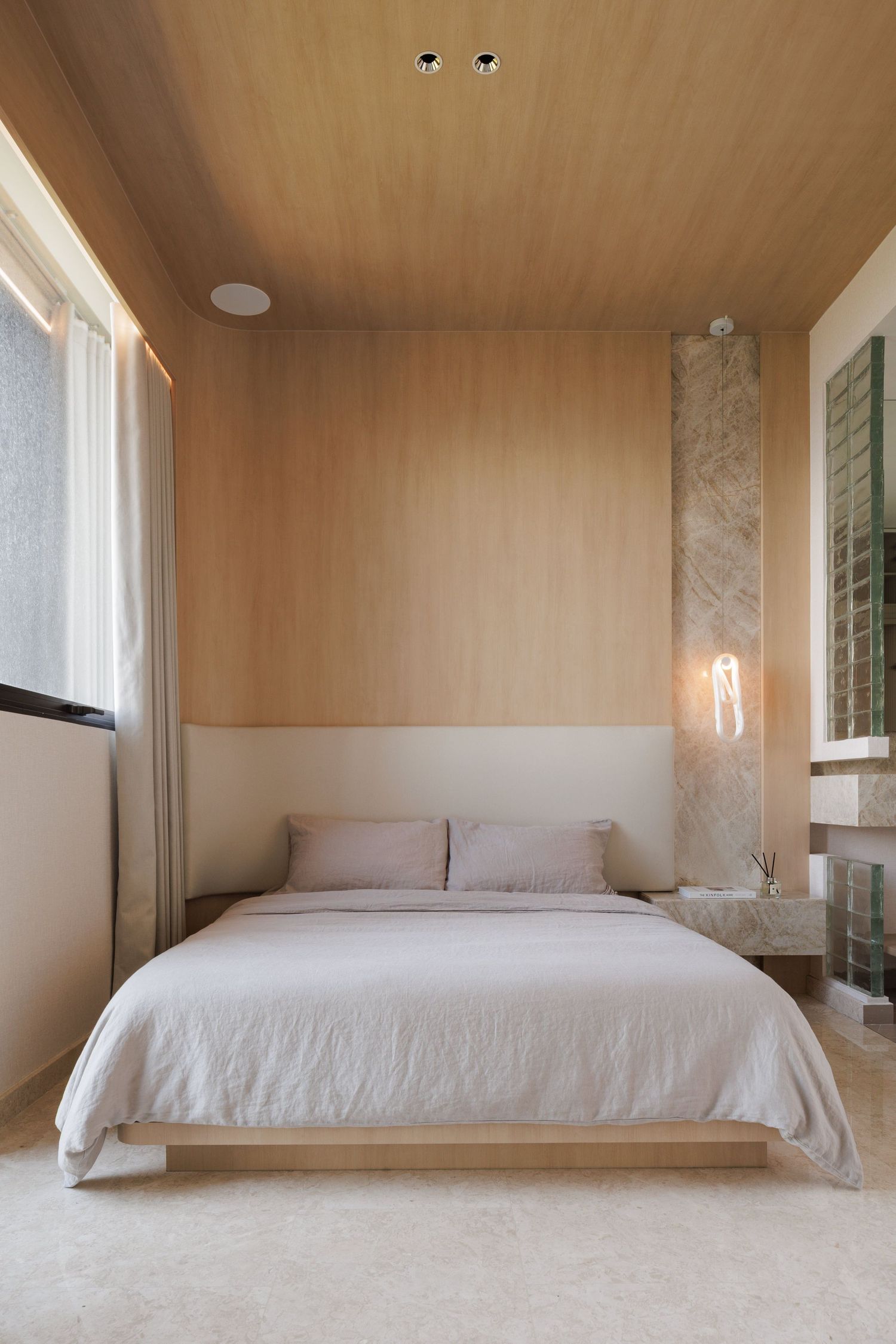 Minimalist bedroom with wood-paneled ceiling, white bedding, and neutral tones featuring modern lighting elements.