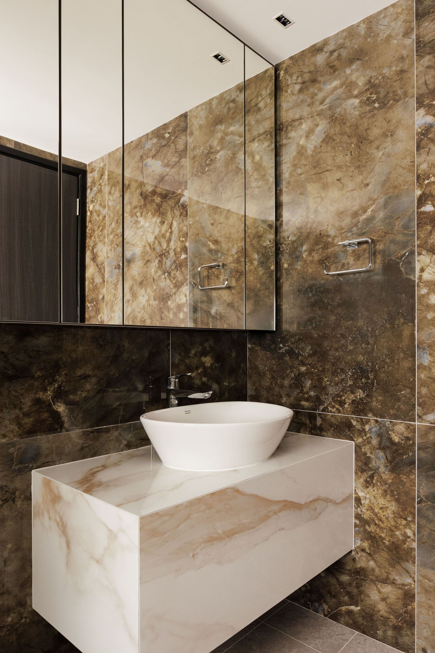 Modern luxury bathroom with brown marble walls, white vessel sink on floating marble vanity, and mirrored medicine cabinet.