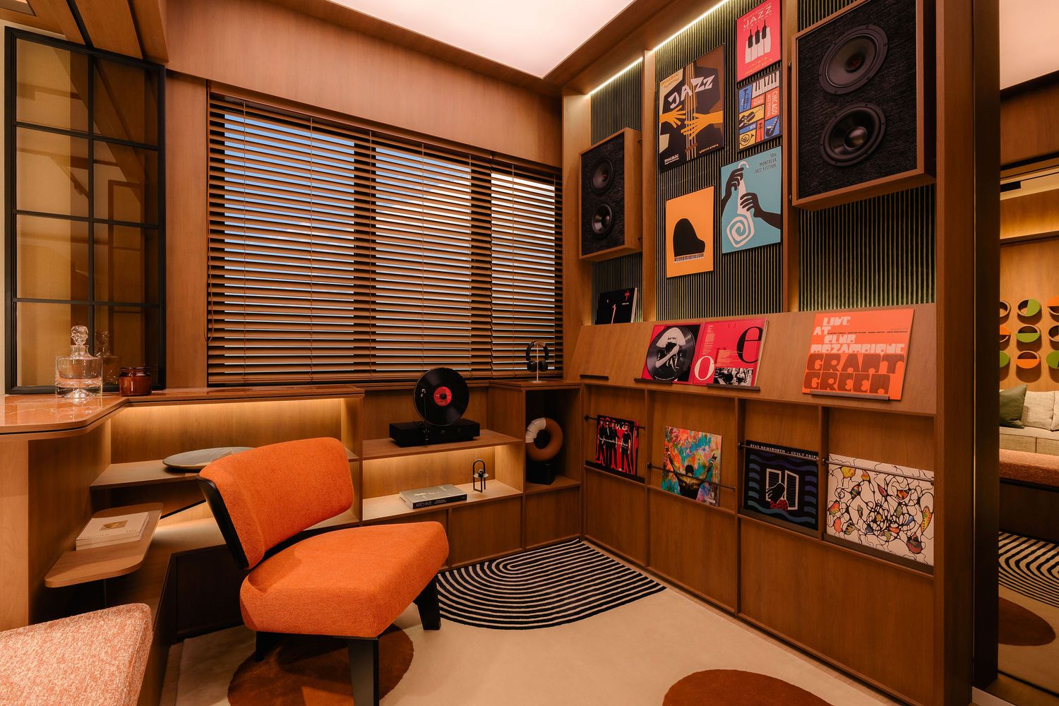 Cozy retro listening room with an orange mid-century chair, vinyl records on wooden shelves, wall-mounted speakers, and window blinds.