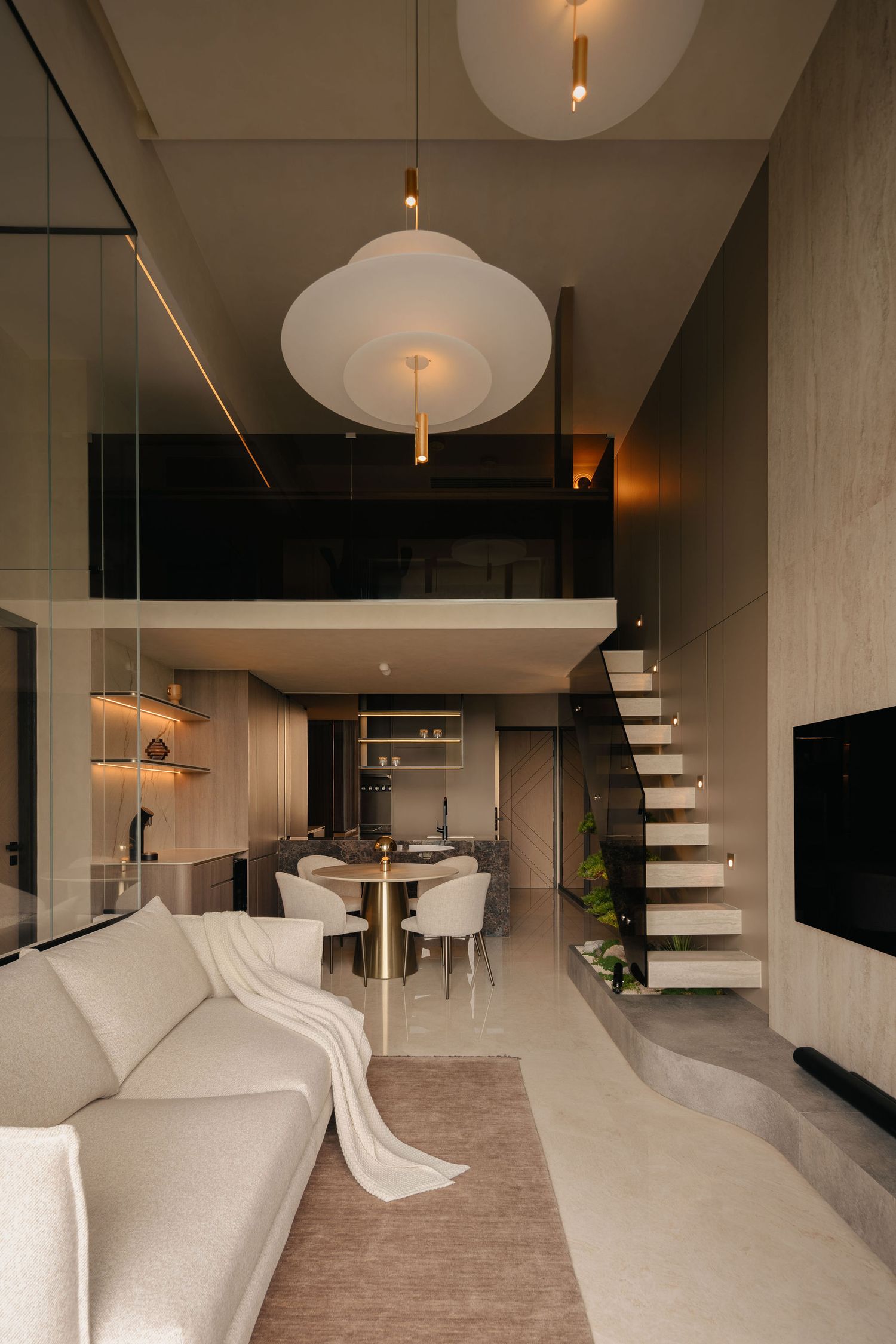 Modern double-height loft interior with a cream sofa, floating staircase, mezzanine, dining table and sculptural pendant lights.