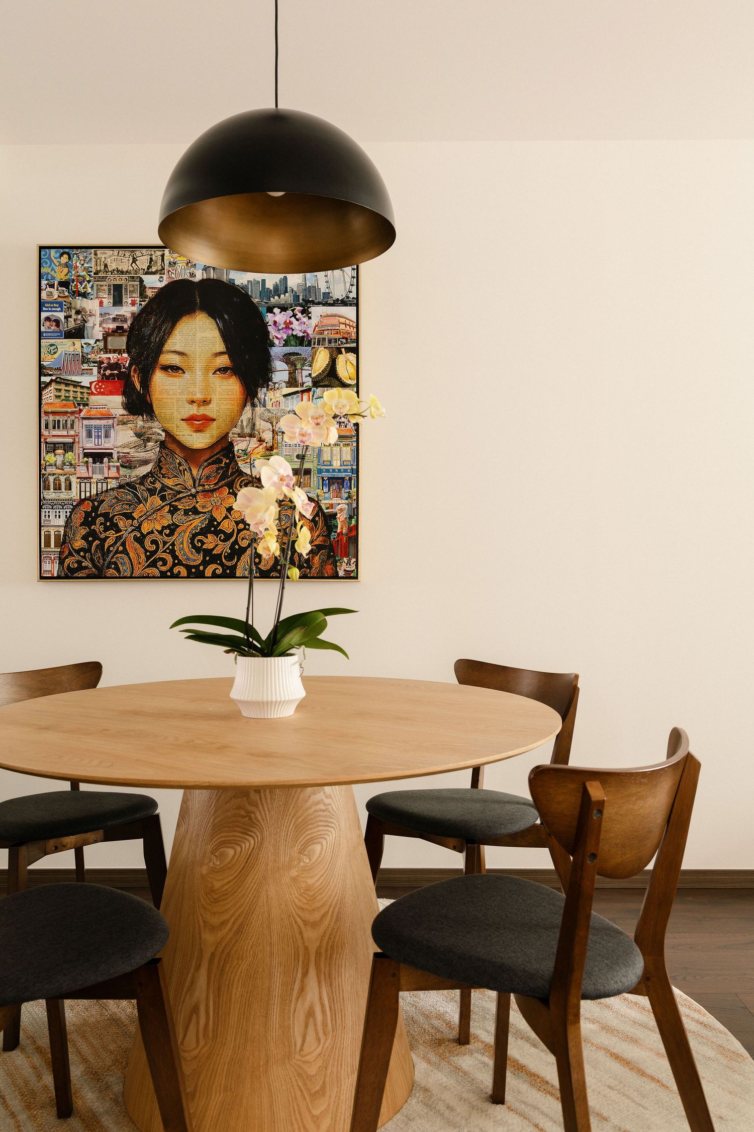 Modern dining room with round wood table, black pendant light, mid-century chairs, and Asian woman portrait artwork on wall.