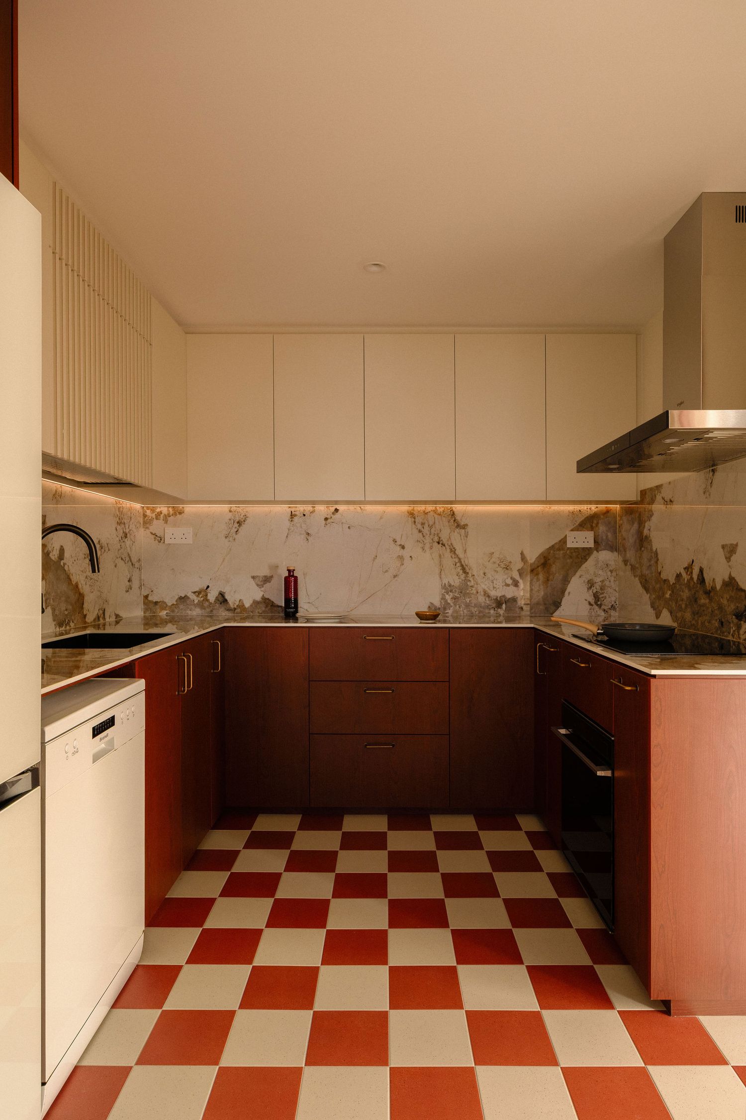 Modern U-shaped kitchen with terracotta and cream checkered floor, rust-red cabinets, marble backsplash, white appliances and a range hood.