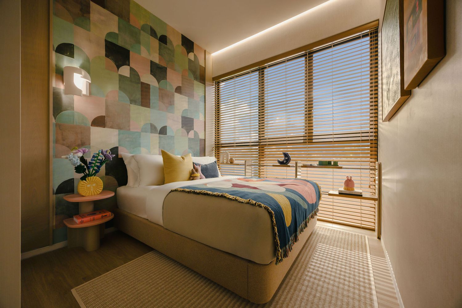 Cozy modern bedroom with a geometric green accent wall, striped blanket, yellow pillows, wooden blinds and a textured area rug.