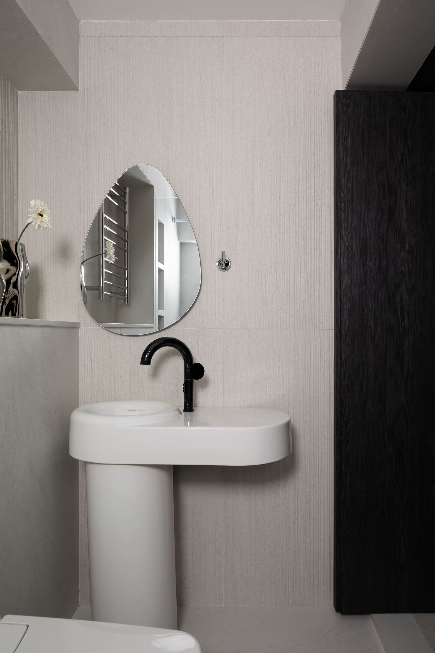 Modern minimalist bathroom with teardrop-shaped mirror, white pedestal sink, and matte black faucet against light gray walls.
