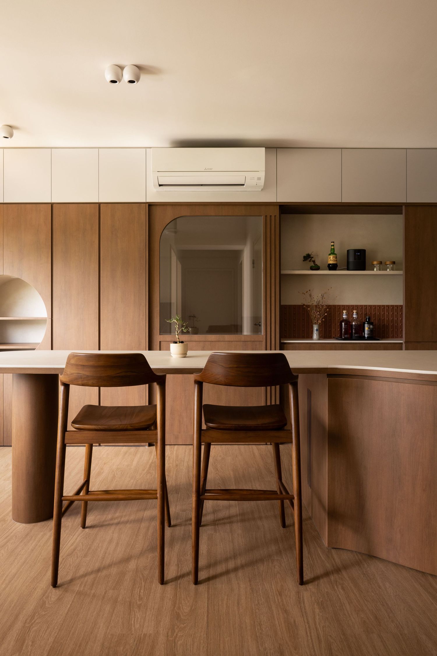 Modern kitchen bar with wooden counter, brown bar stools, and built-in shelving in warm minimalist design.