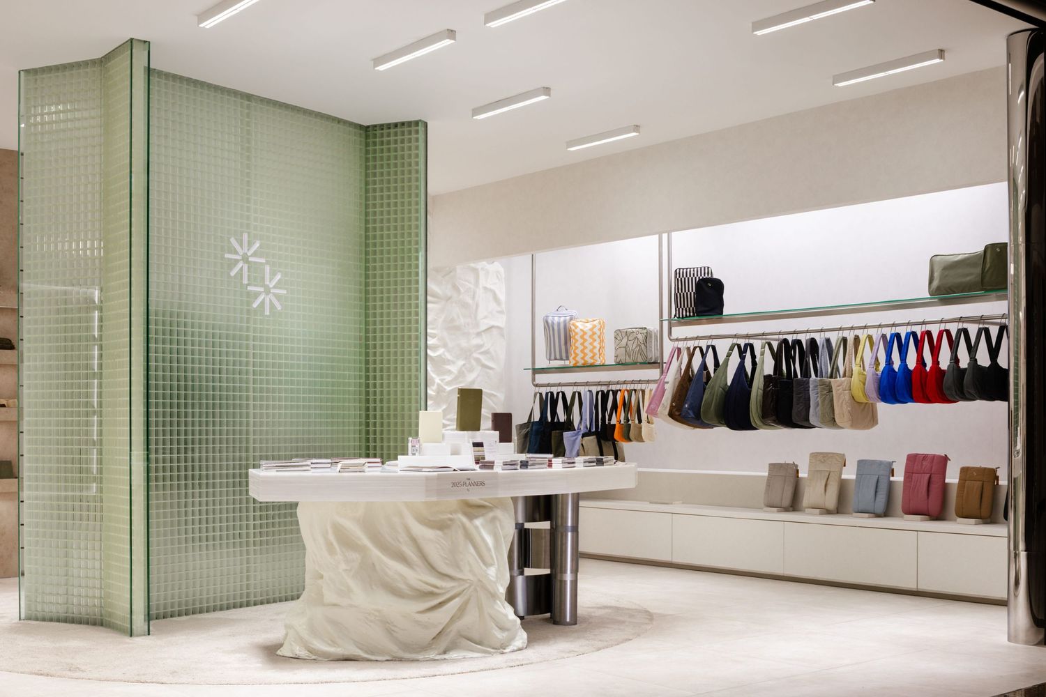 Modern retail store interior with mint green walls, white circular display table, and hanging clothing racks along wall.