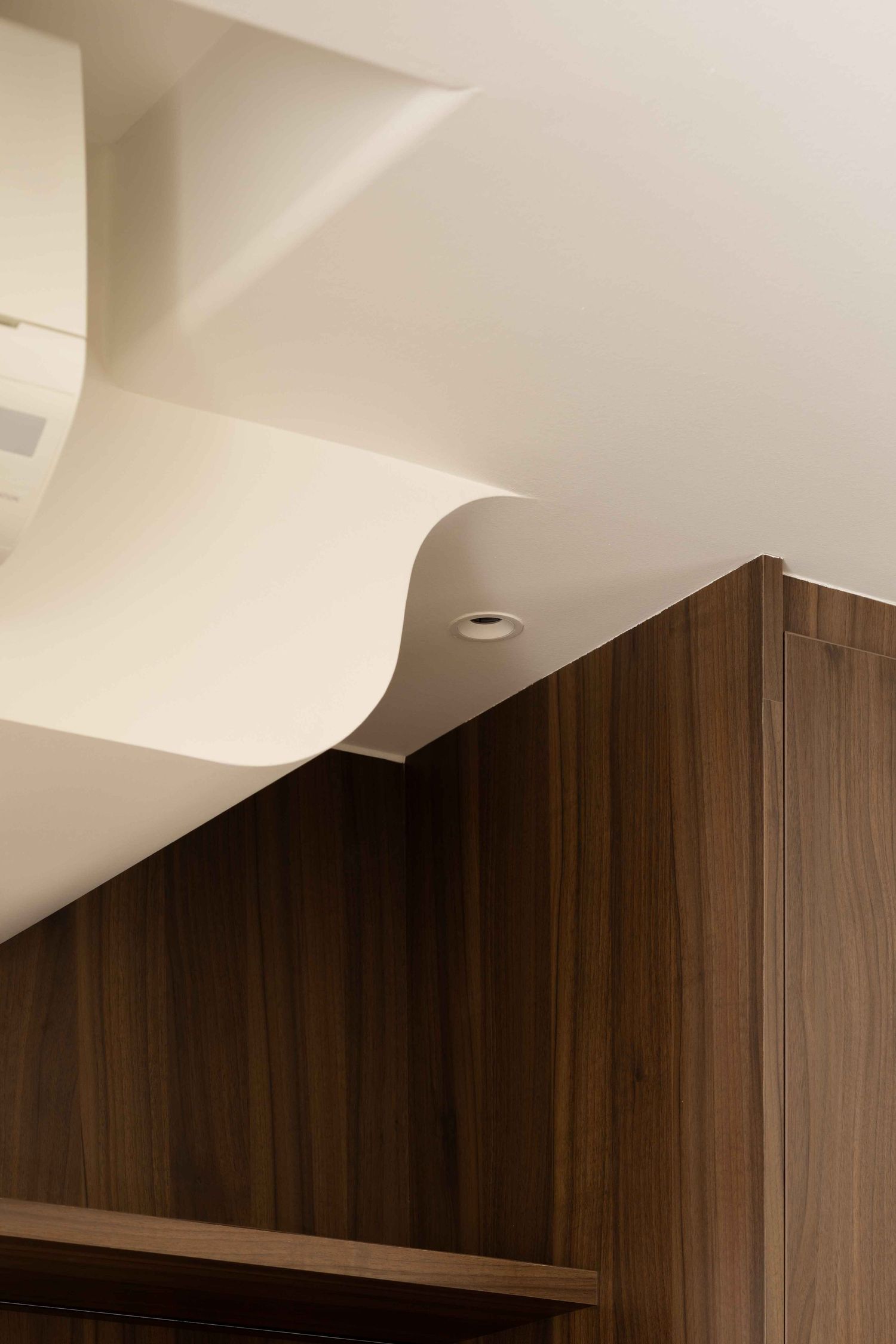 Modern interior design detail showing sleek white ceiling curves meeting dark wood paneling with recessed lighting.