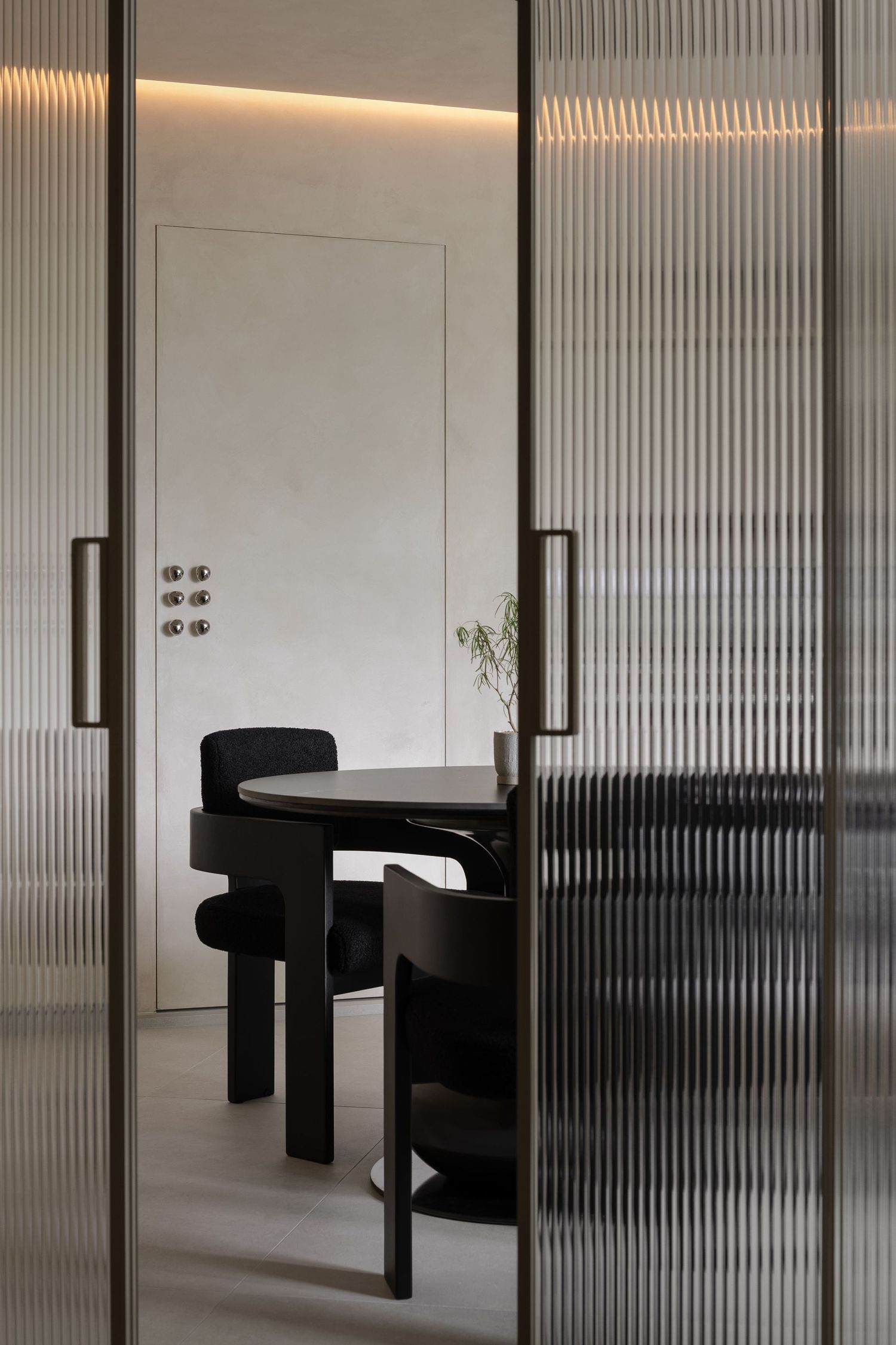 Modern office interior with fluted glass partitions and black curved seating areas in a minimalist design.