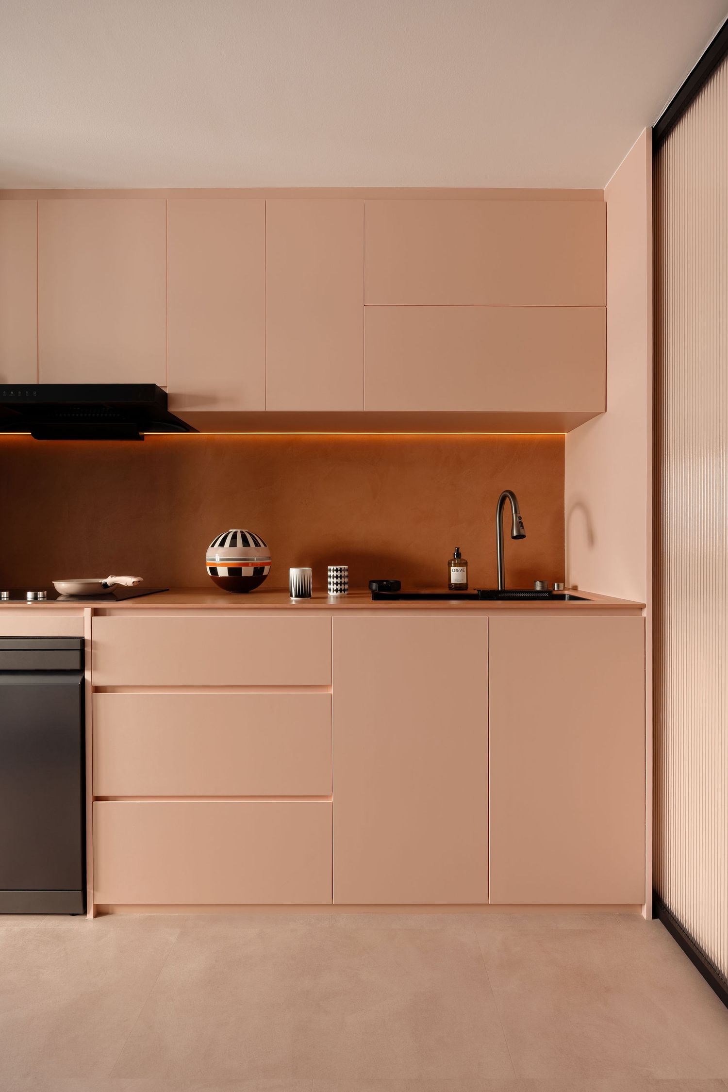 Modern minimalist kitchen with blush pink cabinetry, warm LED under-cabinet lighting, and sleek handleless drawers.