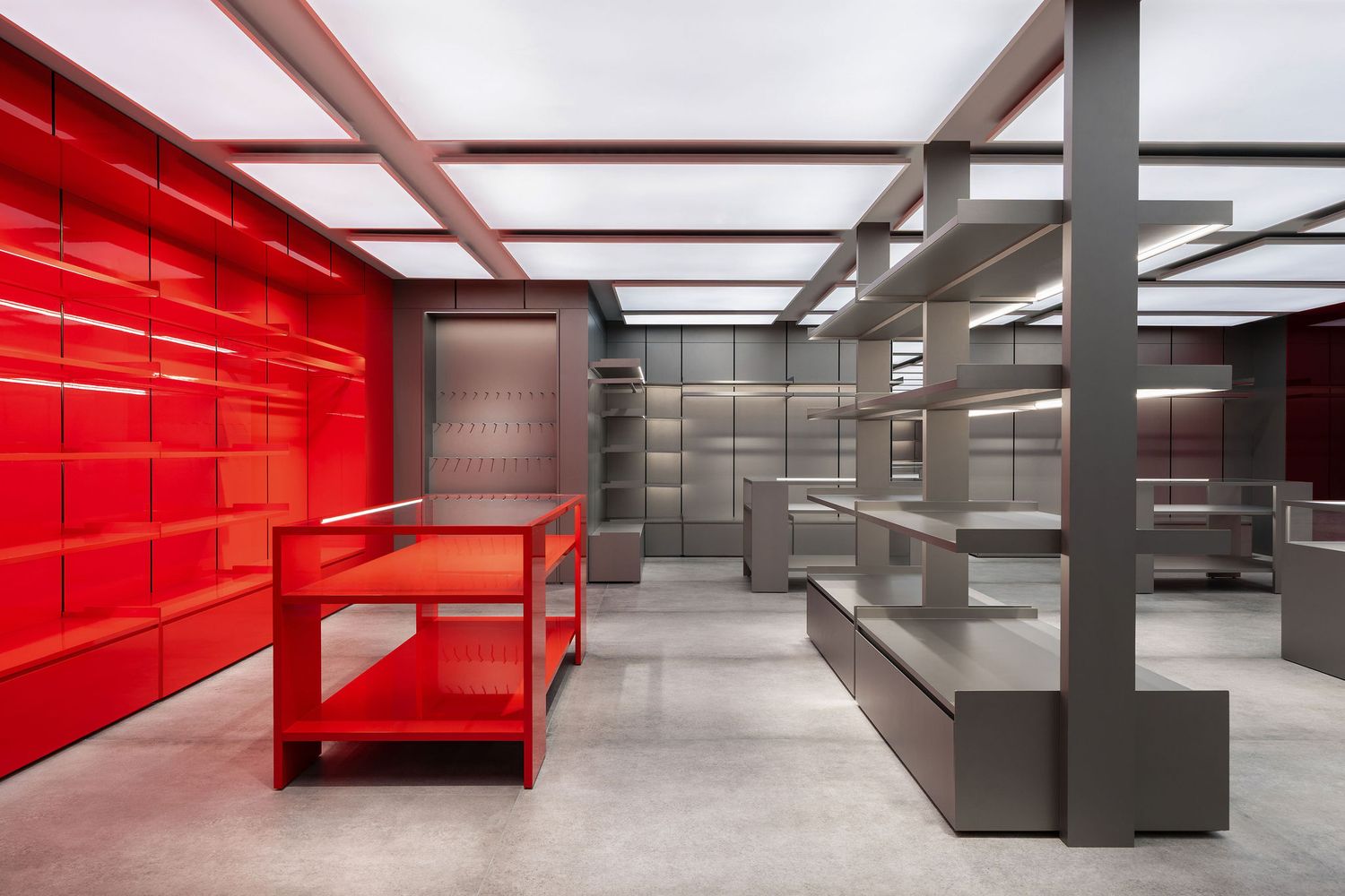 Modern retail store interior with bold red shelving wall, red display table, and sleek gray metal shelving units.