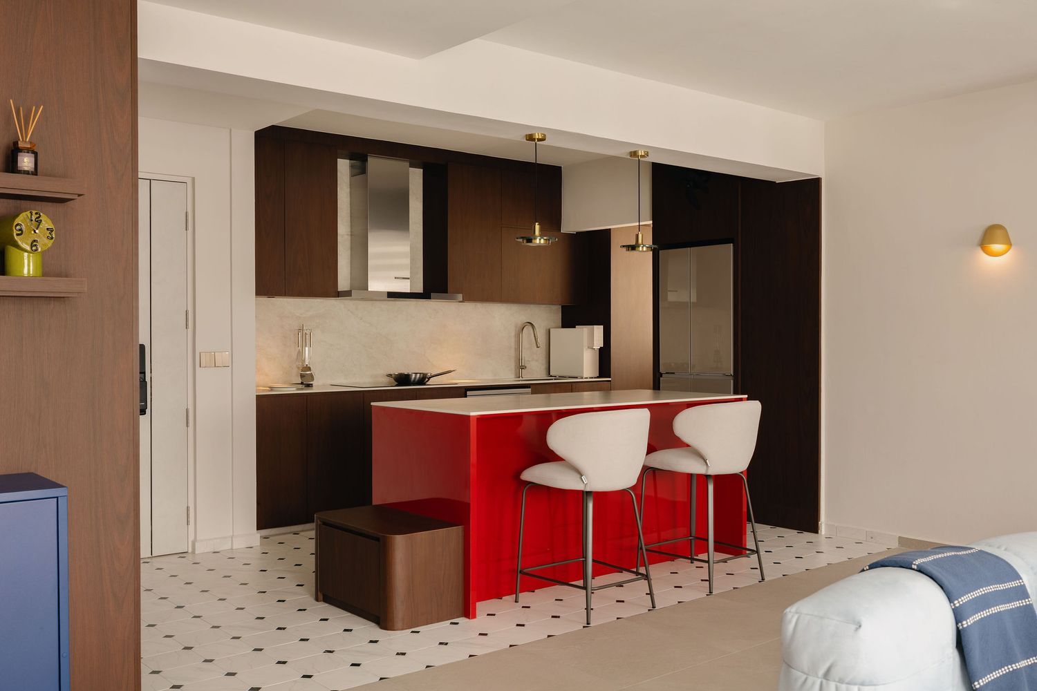 Modern studio kitchen with red island, white bar stools, dark wood cabinets, and black-and-white checkered tile floor.