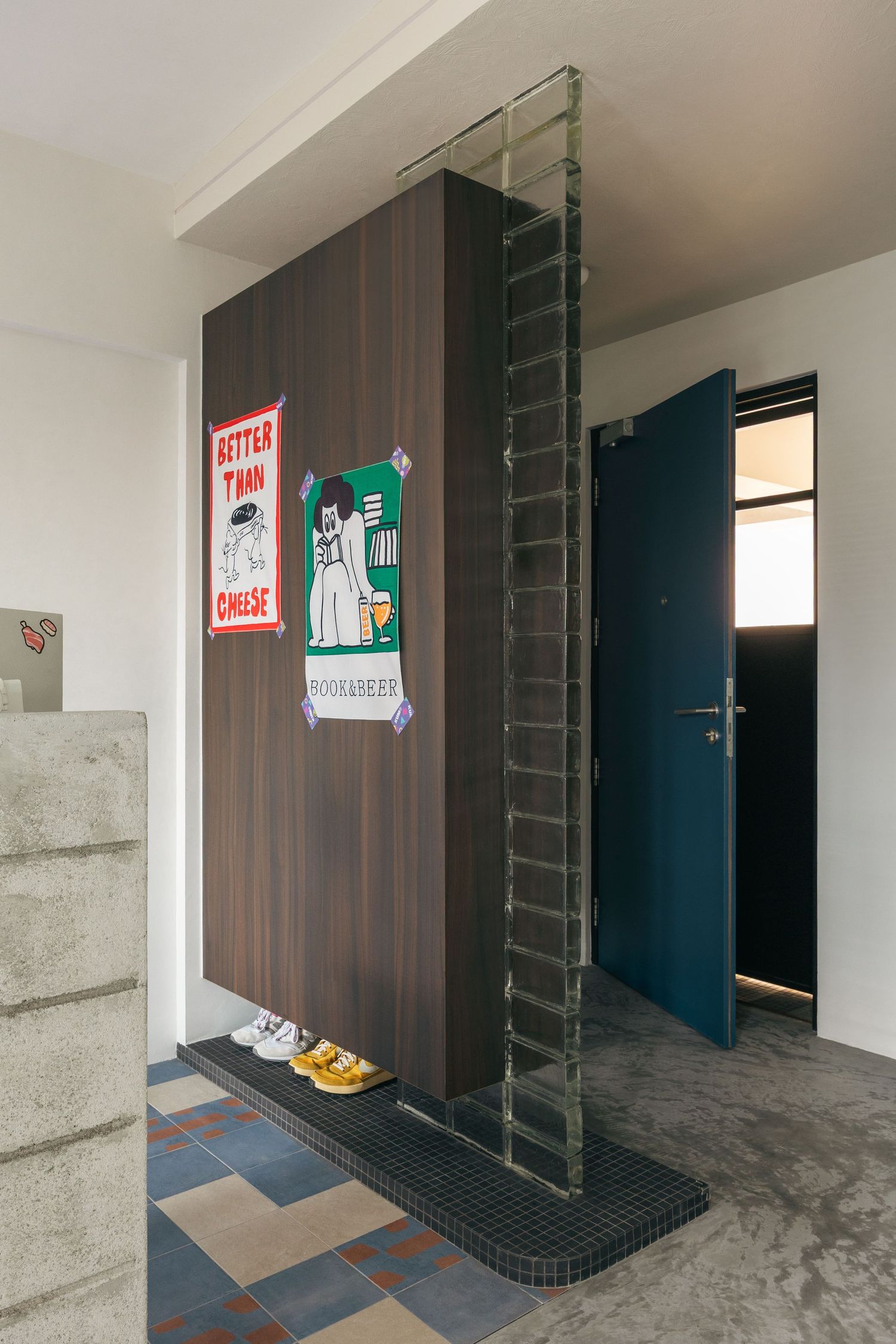 Modern entryway with dark wood panel, glass ladder, teal door, colorful tile floor, and decorative posters in a contemporary interior.