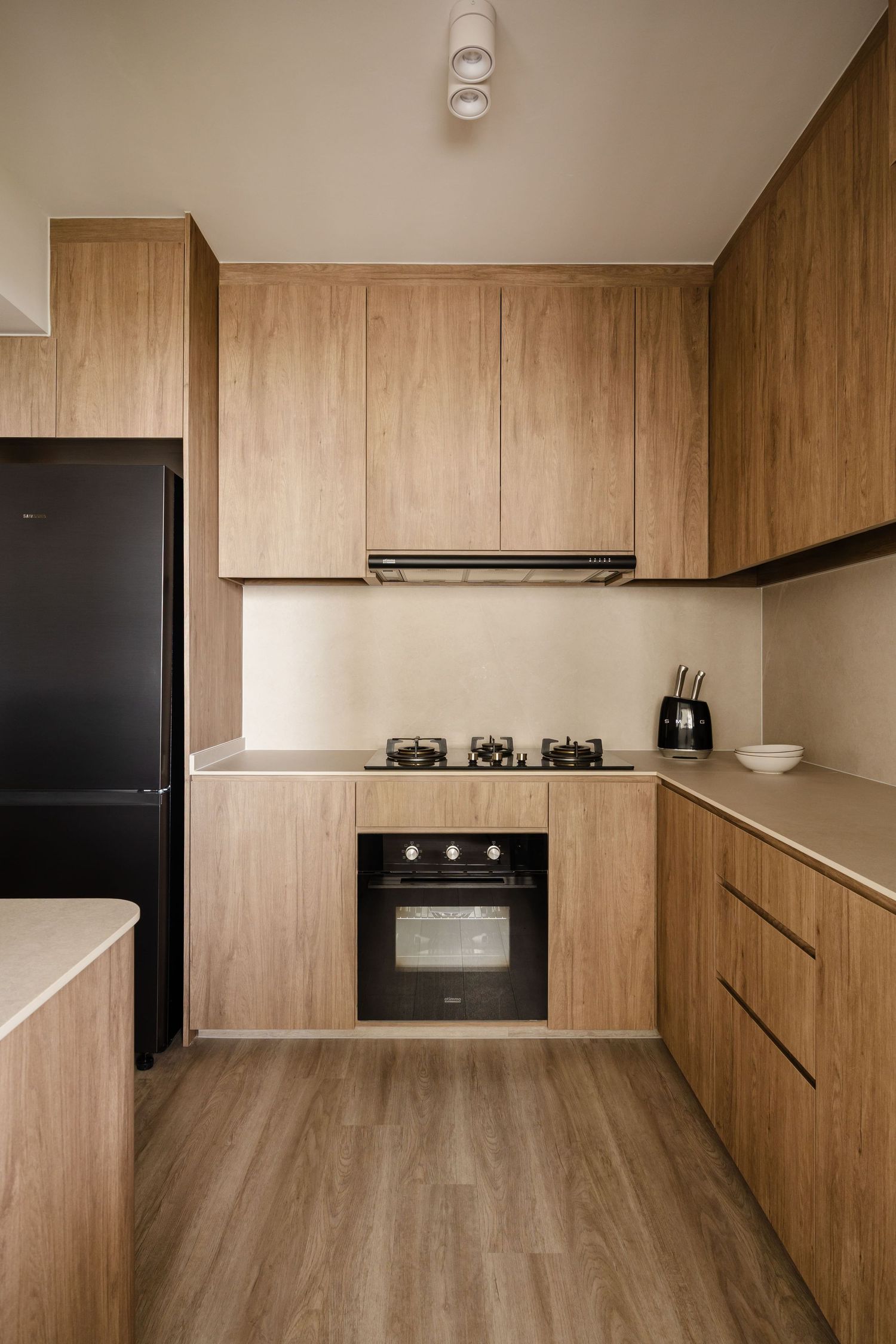 Modern wood-paneled kitchen with sleek black appliances and clean lines showcases minimalist design in warm neutral tones.