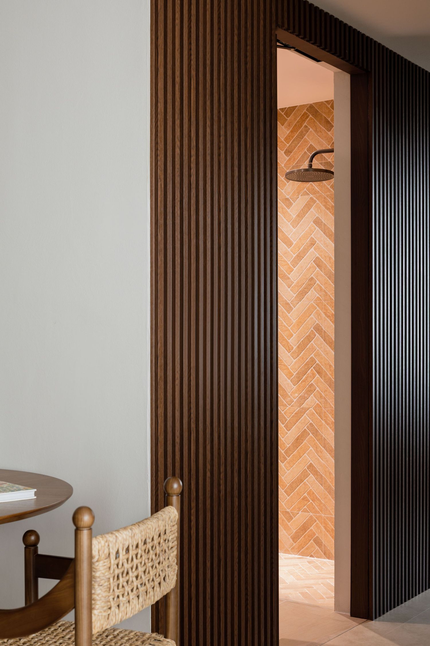 Modern interior with black slatted wall panel and wood herringbone tile floor leading to bathroom doorway.