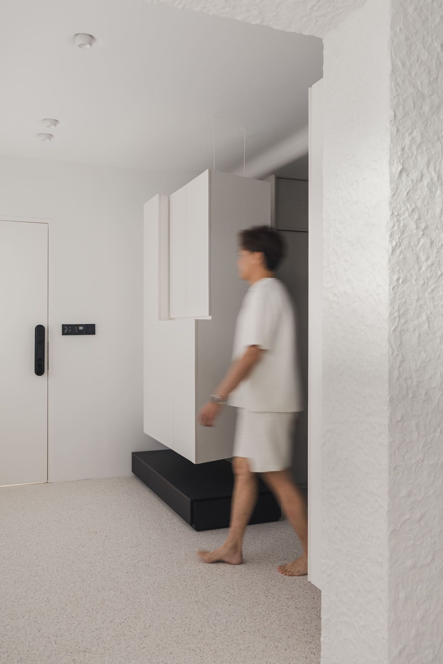 Person walking barefoot through a minimalist white apartment interior with modern cabinetry and clean lines.