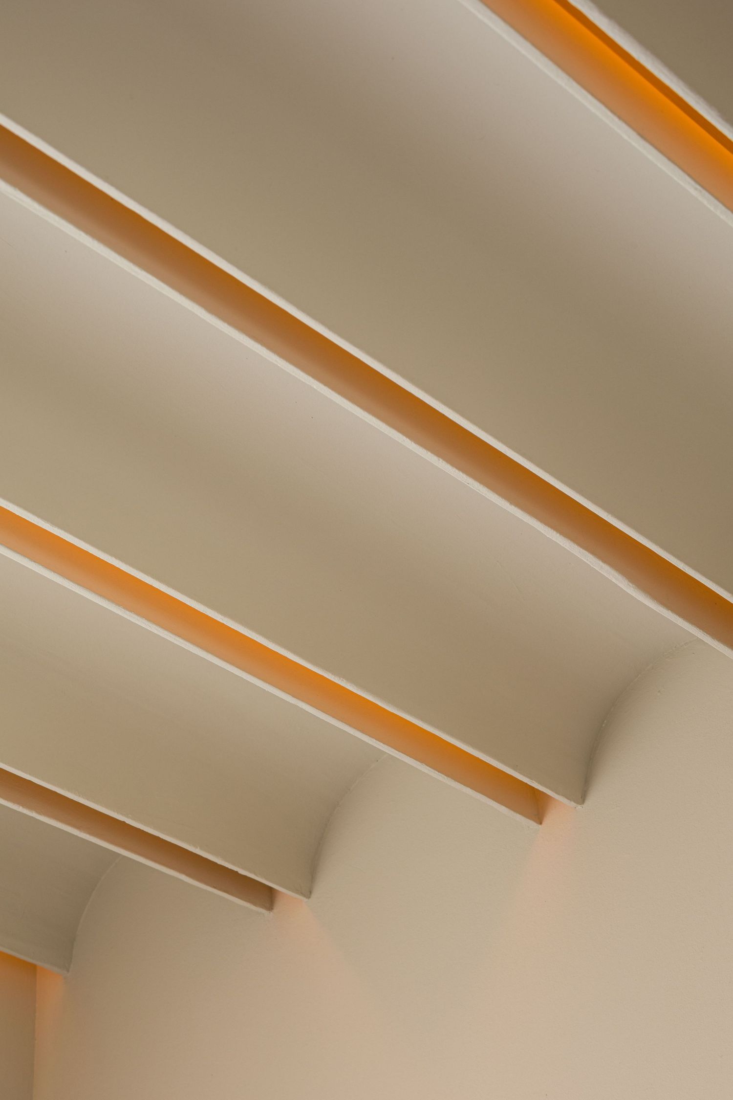 Modern ceiling with diagonal recessed panels featuring warm amber LED strip lighting on beige architecture.