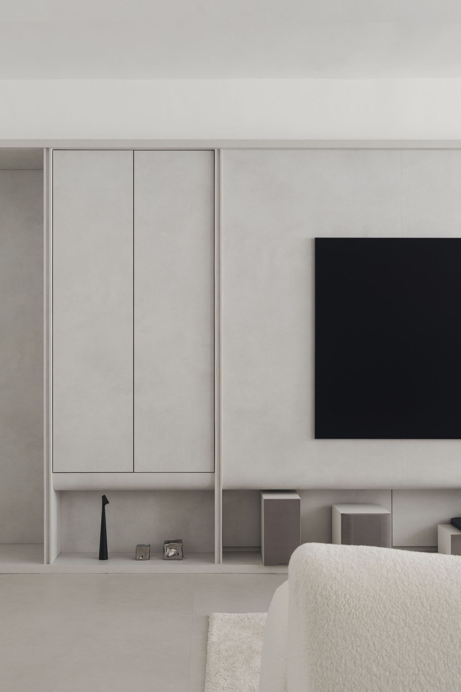 Minimalist living room with white built-in cabinets, wall-mounted TV, and neutral tones throughout.
